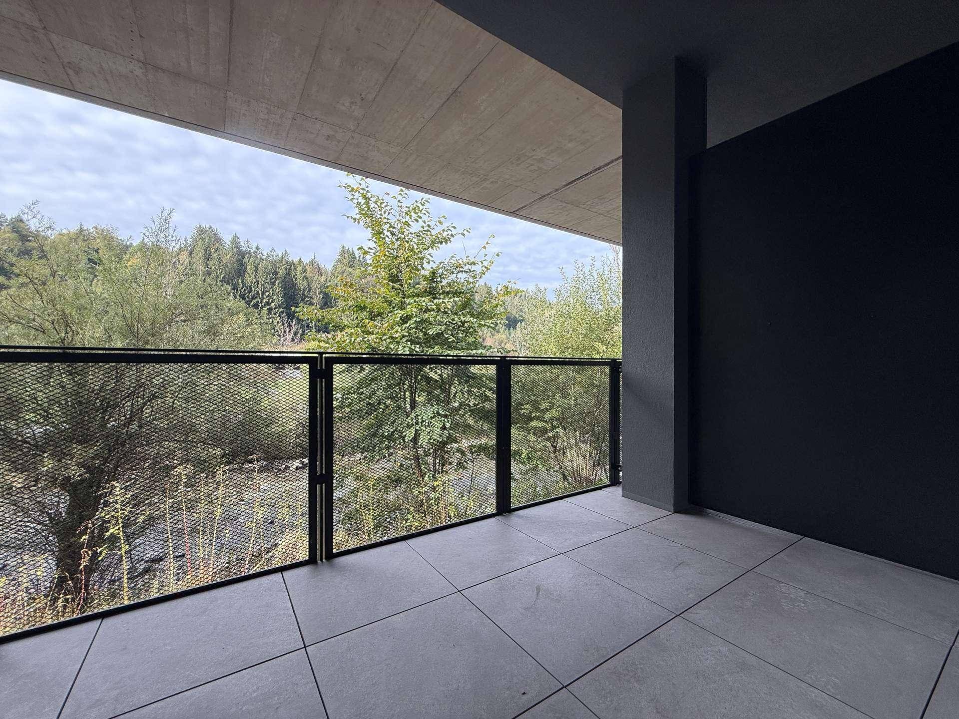 Moderner Balkon mit Fliesenboden und Metallgeländer, bietet einen grünen Ausblick auf die Natur.