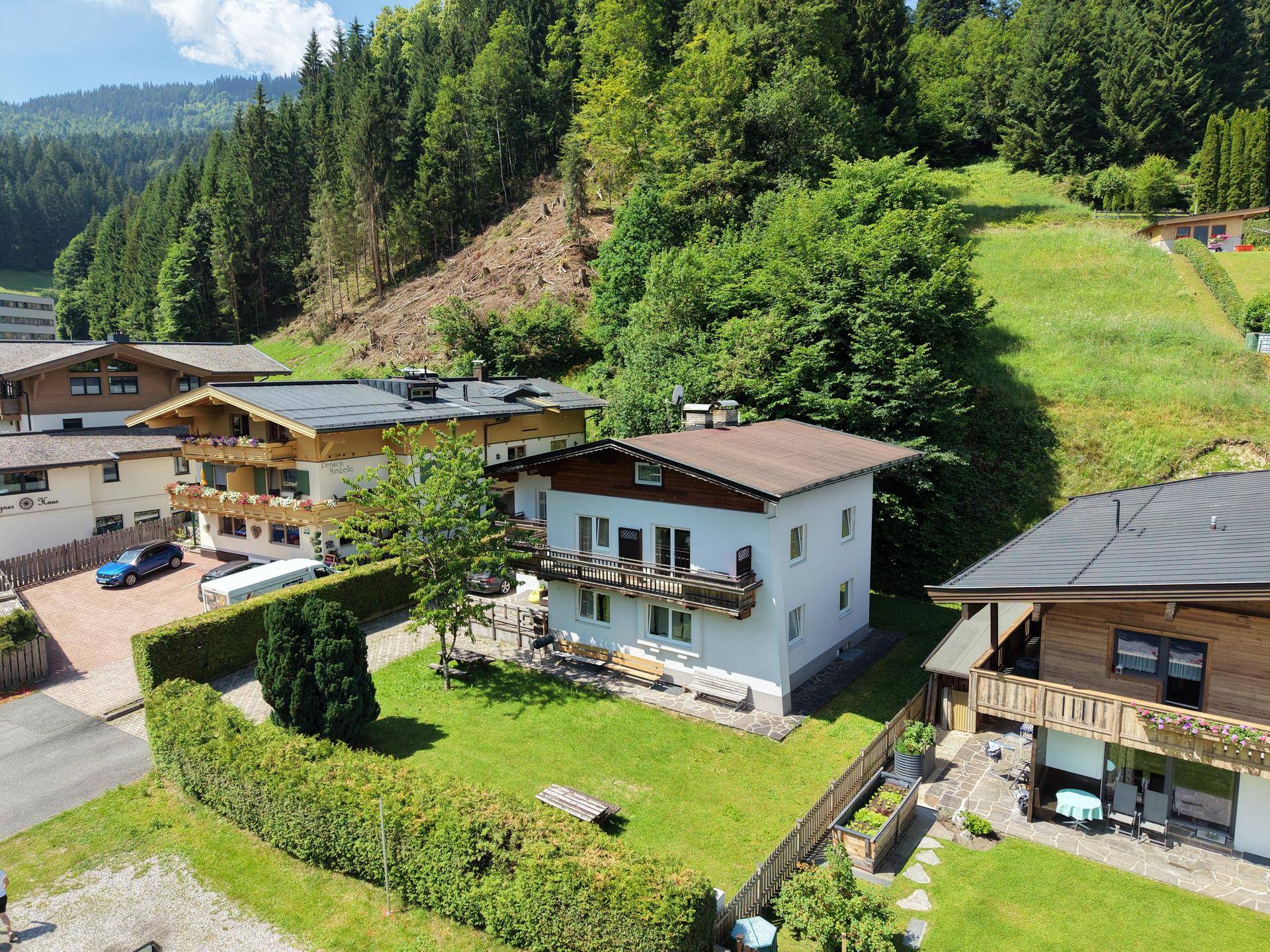 Hausfassade mit Balkon und gepflegtem Garten, umgeben von üppiger Berglandschaft.
