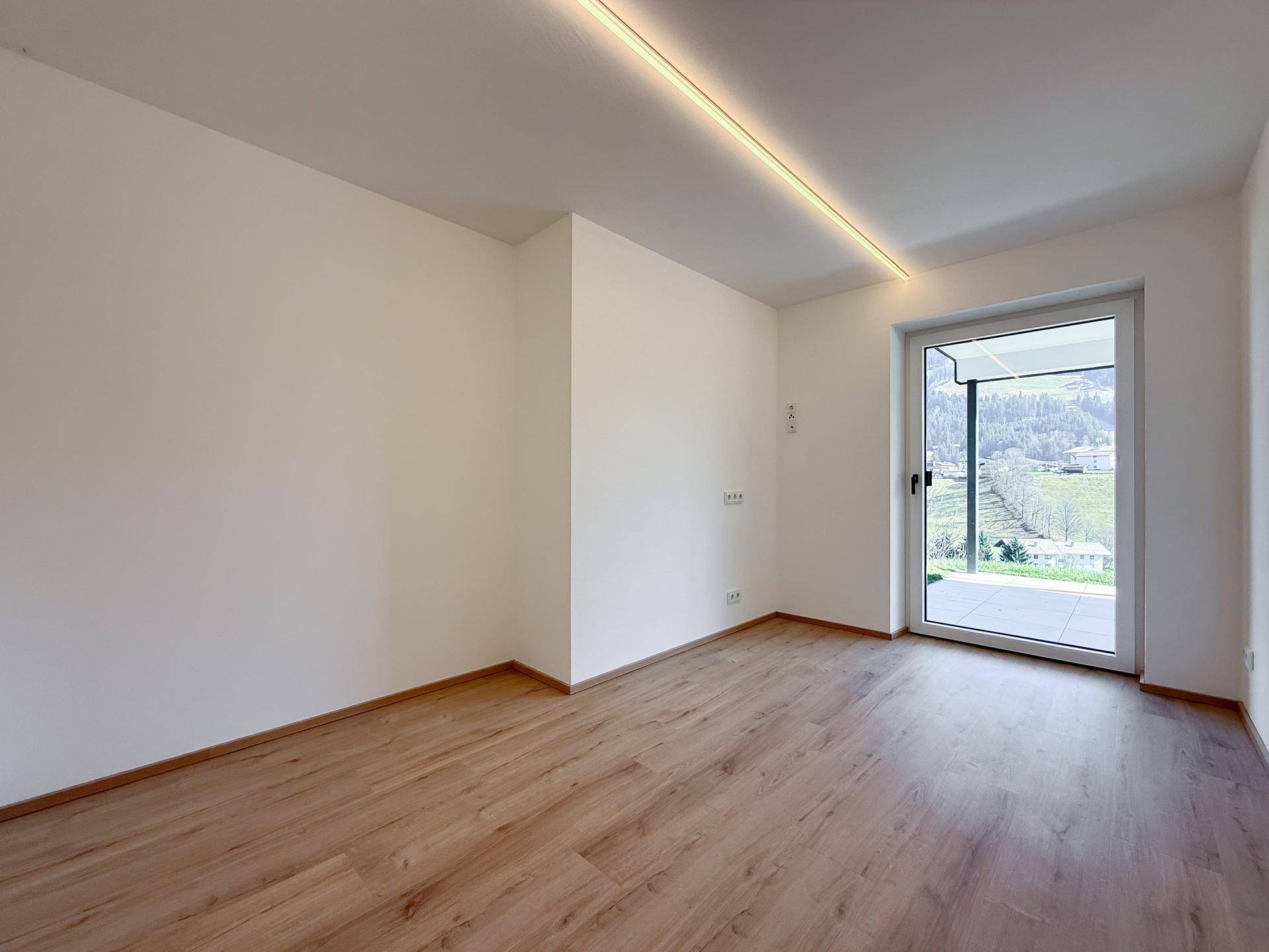 Heller, leerer Raum mit Holzboden und Zugang zu einem Außenbereich.