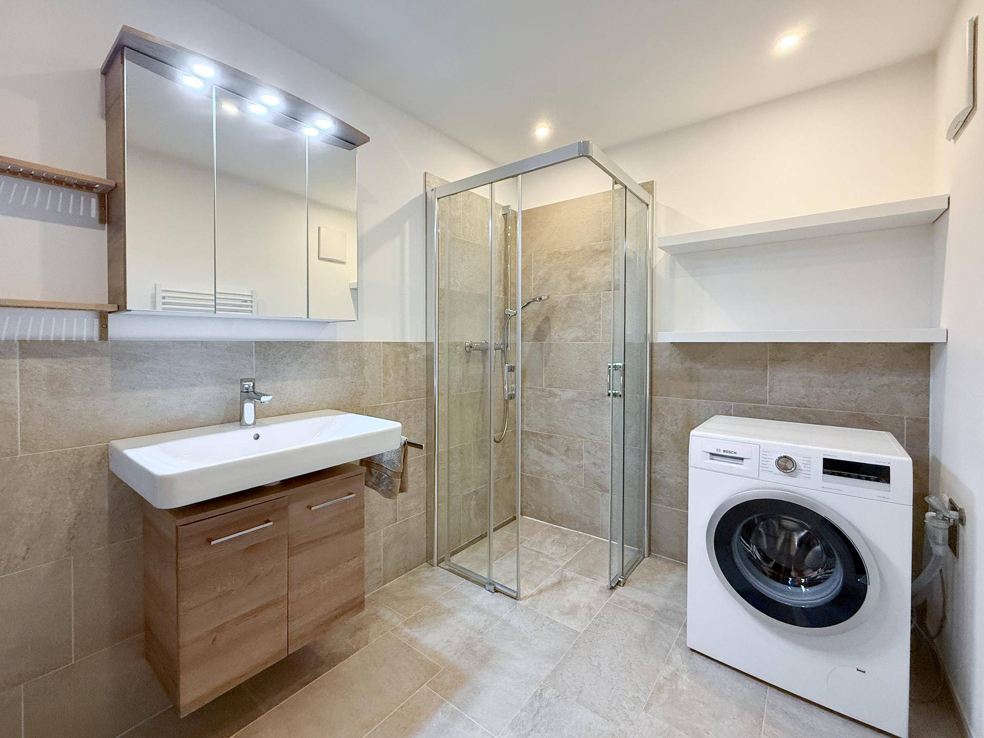 Modernes Badezimmer mit Duschkabine, Einzelwaschbecken und Waschmaschine.