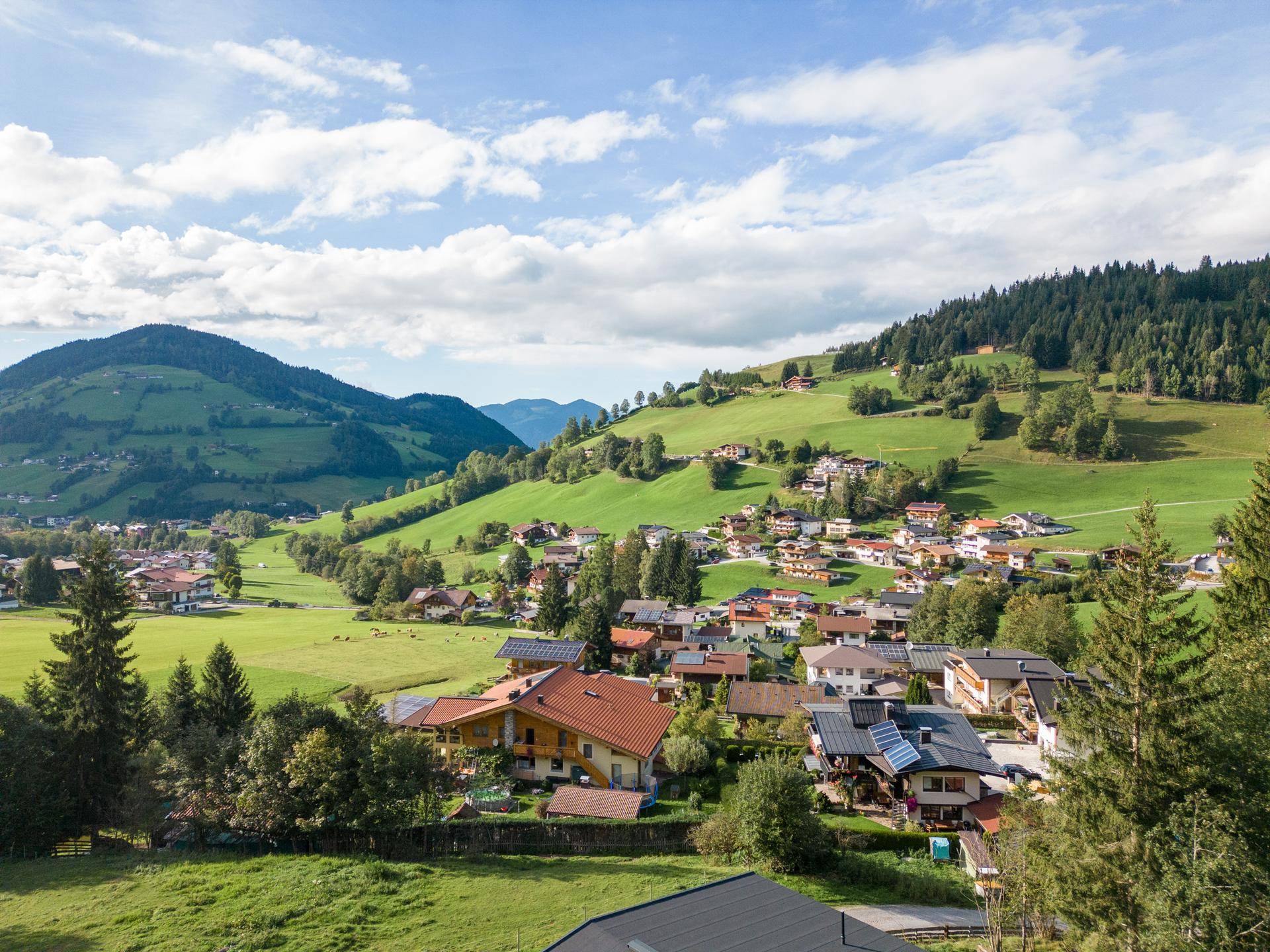 Malerisches Dorf in einem grünen Tal, umgeben von sanften Hügeln und Bergen unter blauem Himmel.