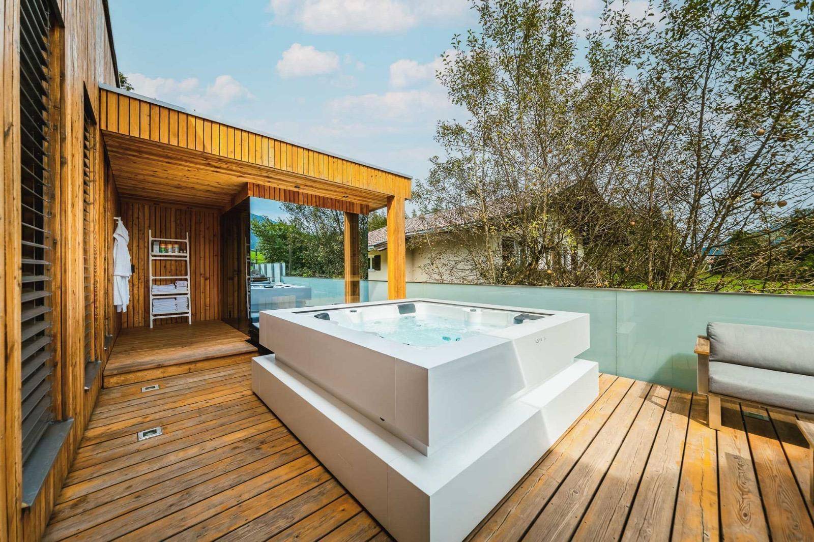 Sonniger Außenbereich mit modernem Whirlpool auf Holzdeck und Blick auf die Umgebung.