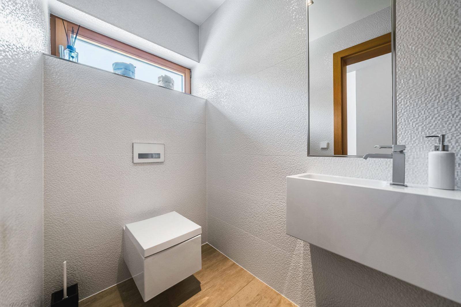 Kleines Gäste-WC mit modernem Design, wandmontierter Toilette und Fenster.