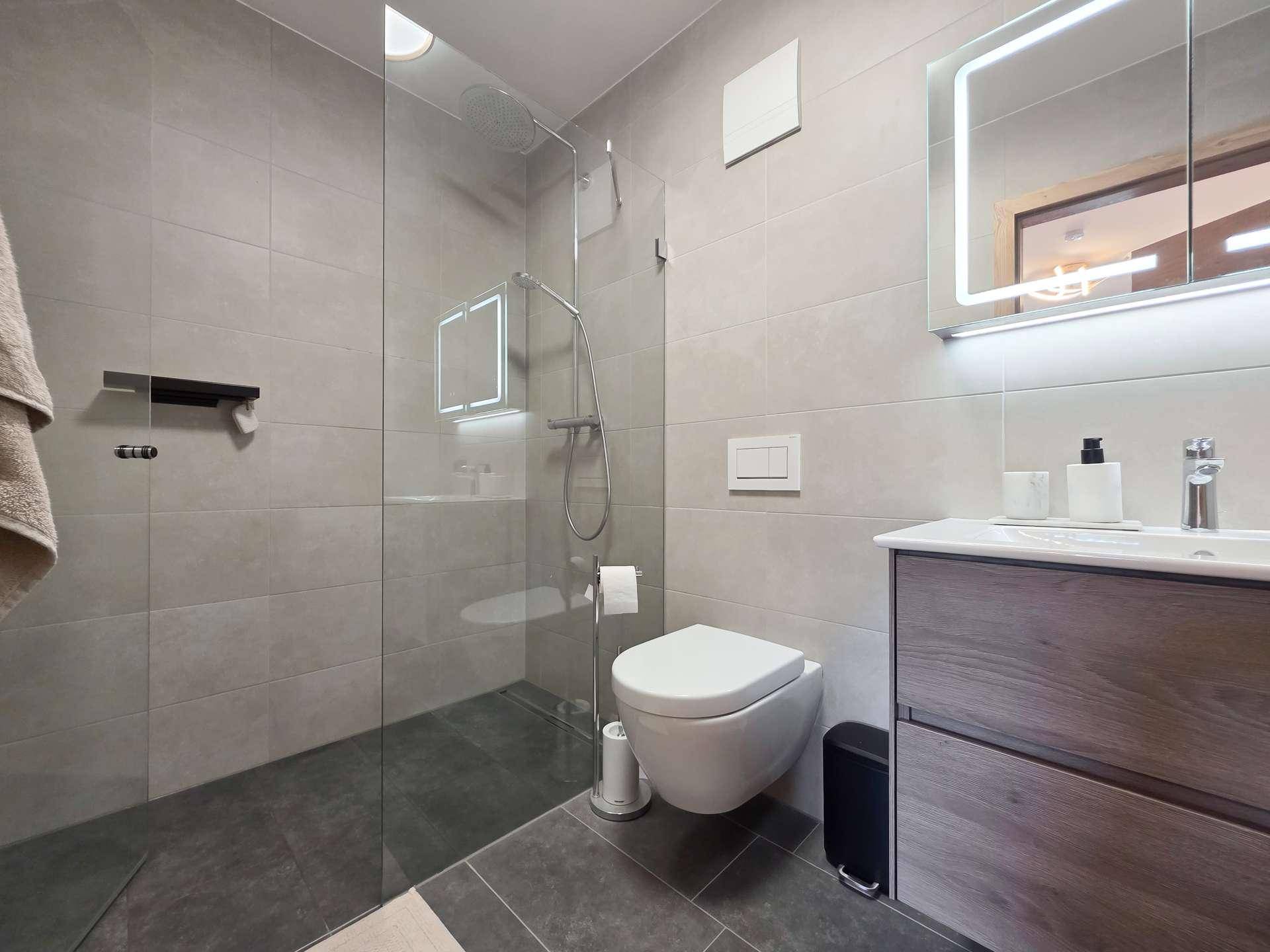 Modernes Badezimmer mit ebenerdiger Dusche, Wand-WC und beleuchtetem Spiegelschrank.