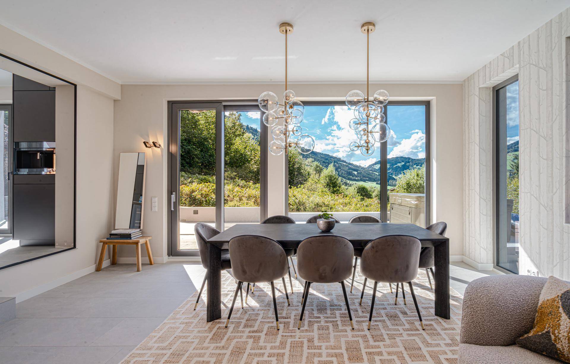 Heller Essbereich mit großem Tisch, modernen Leuchten und weitem Blick auf die Berge und Natur.