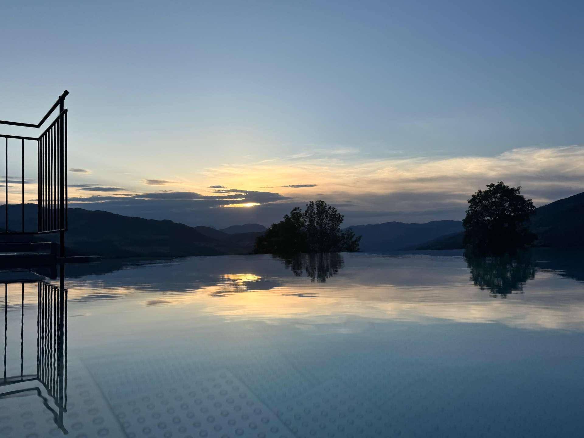 Infinity-Pool bei Sonnenuntergang mit ruhiger Wasseroberfläche und weitem Blick auf die Berge.