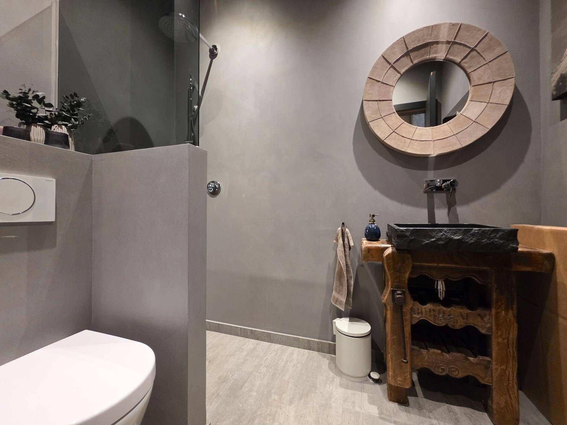 Elegantes Badezimmer mit modernem WC, einzigartigem Holzwaschtisch und runden Spiegel, in Grautönen gehalten.