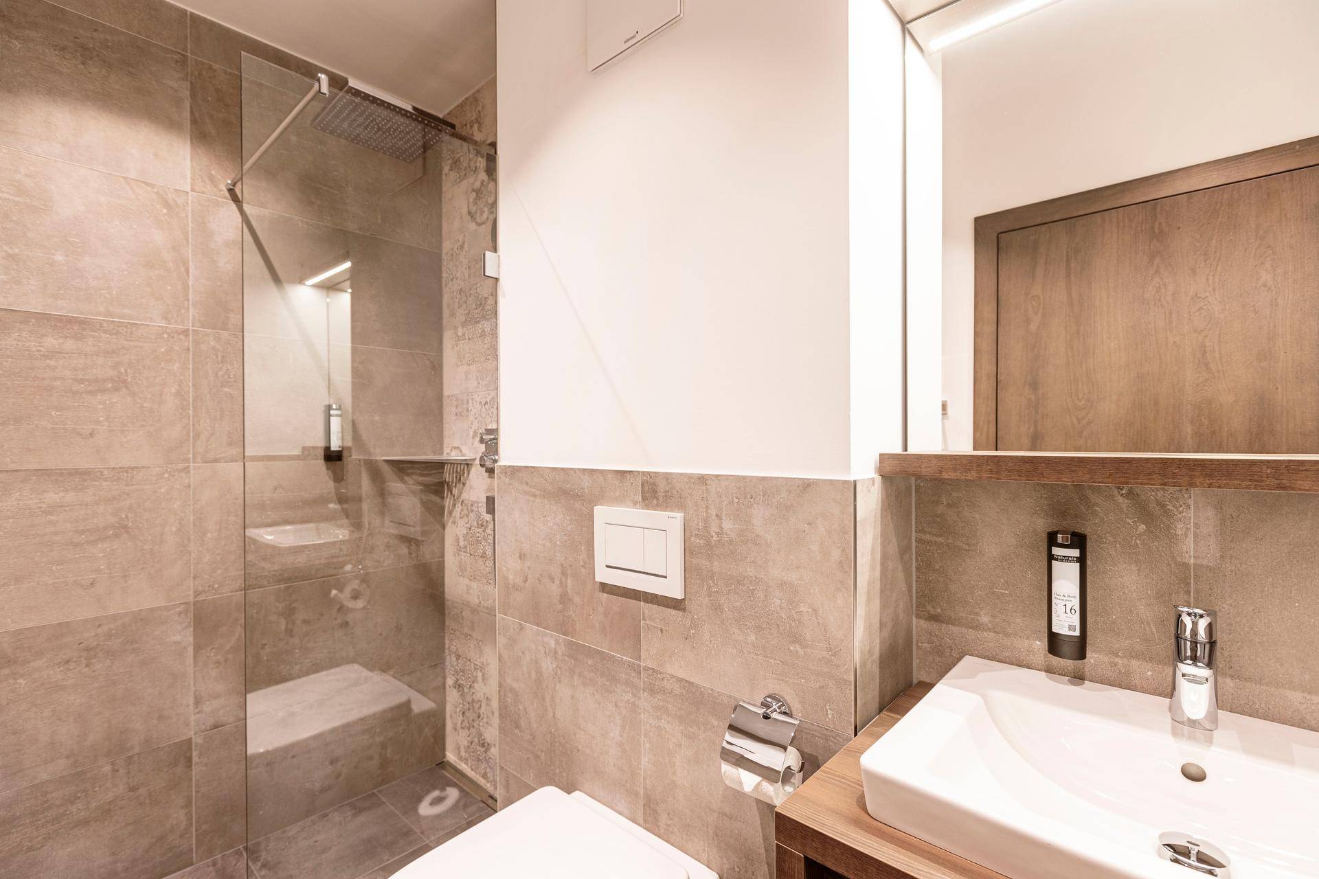 Zeitgemäßes Badezimmer mit WC, Waschbecken und einer geräumigen begehbaren Dusche mit Glasabtrennung.