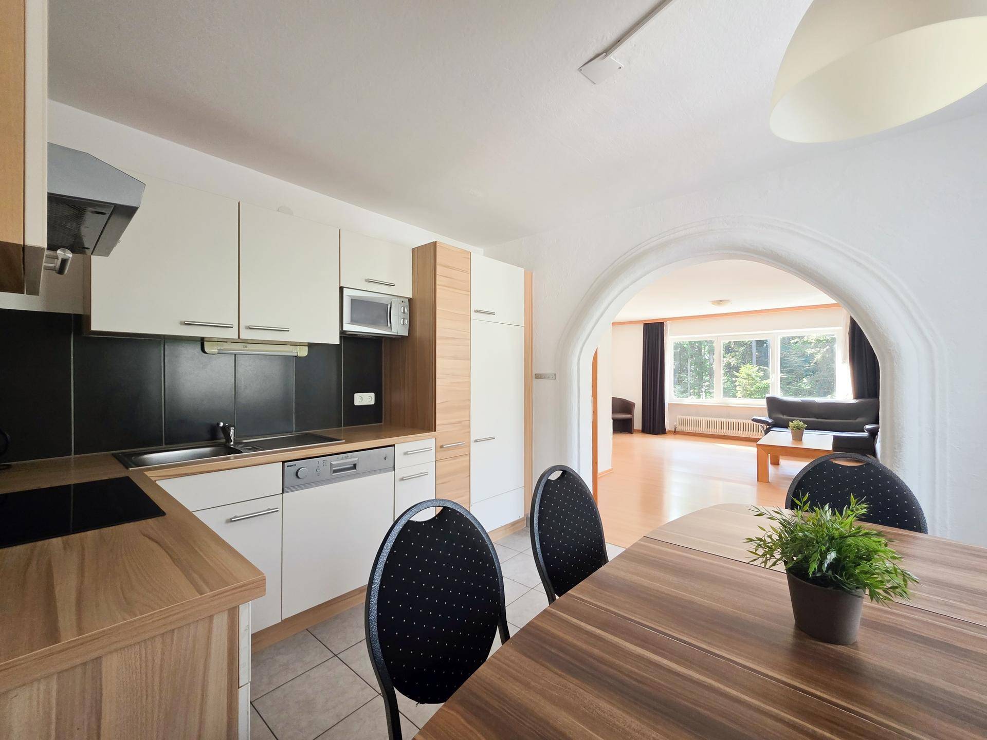 Moderne Küche mit weißen Schränken, Holzarbeitsplatten und Essbereich, offen zum Wohnzimmer.