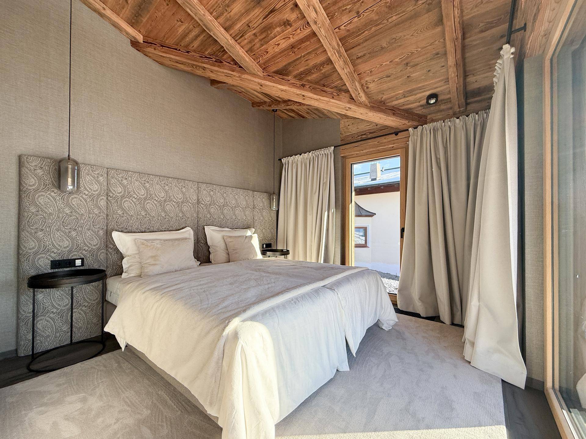 Helles Schlafzimmer mit Holzbalkendecke, gemütlichem Bett und direktem Zugang nach draußen.