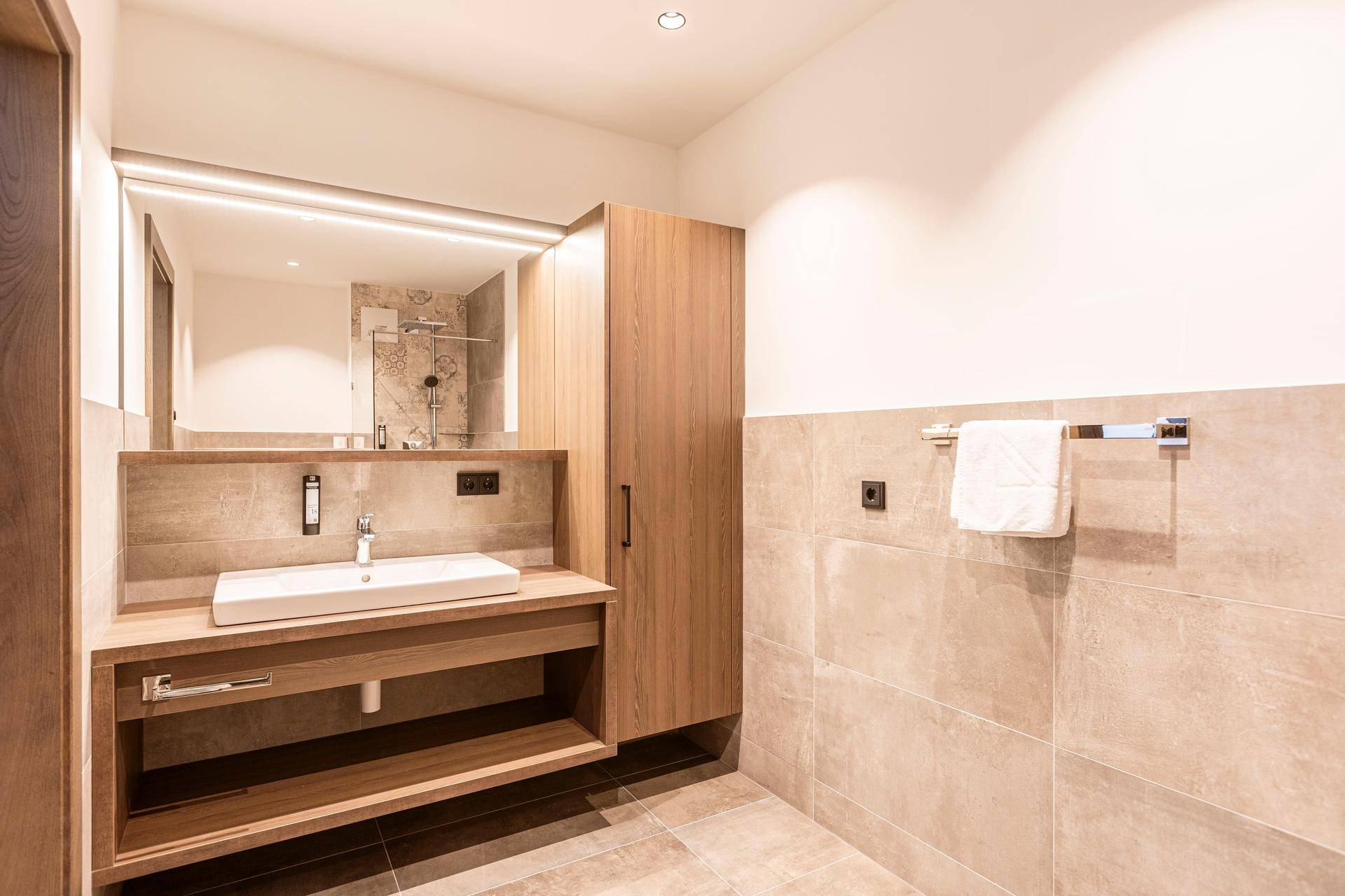 Modernes Badezimmer mit großformatigen Fliesen, Waschtisch und beleuchtetem Spiegel.