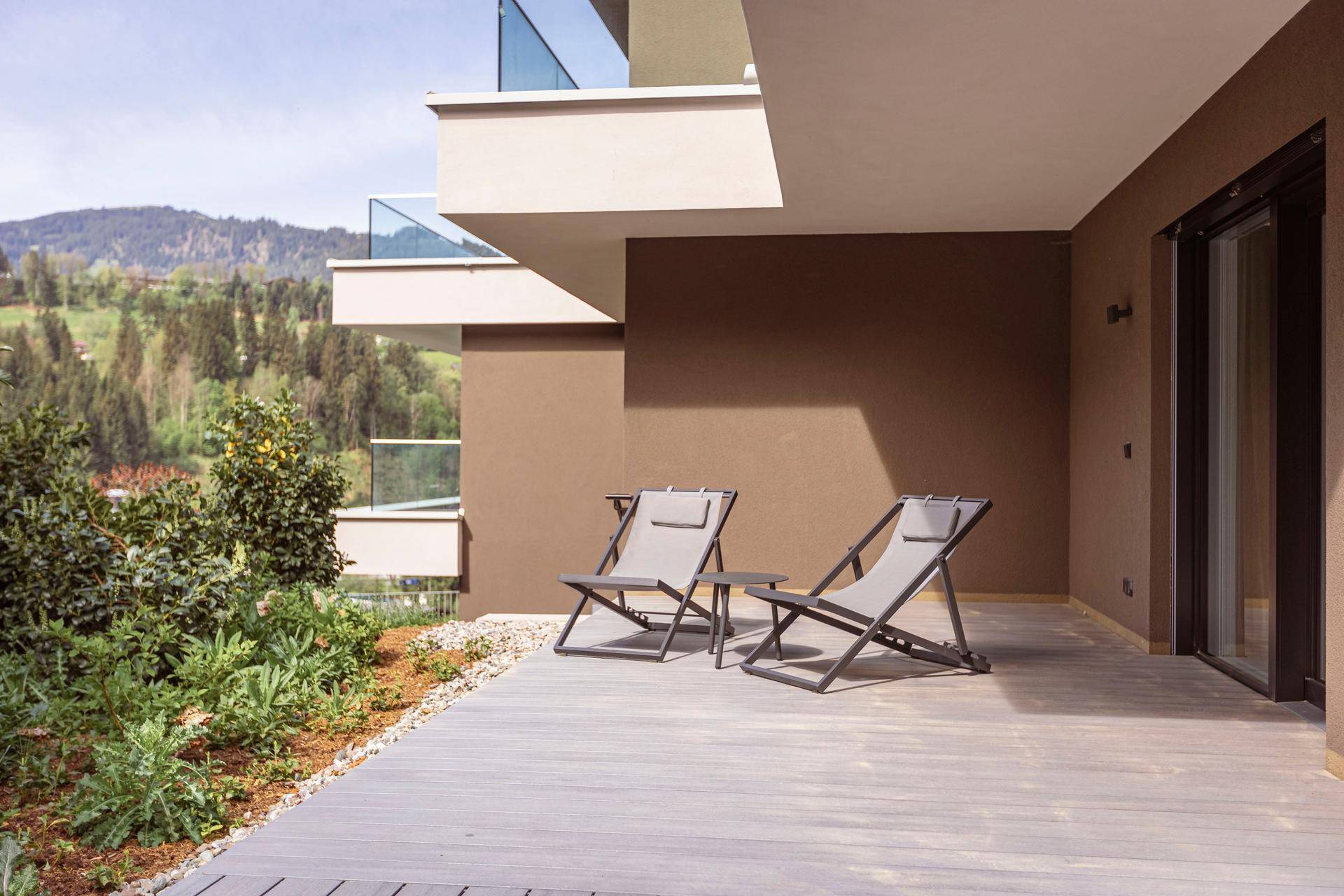 Ebenerdige Terrasse mit Holzdeck und Liegestühlen, umgeben von Pflanzen und mit Bergblick in der Ferne.
