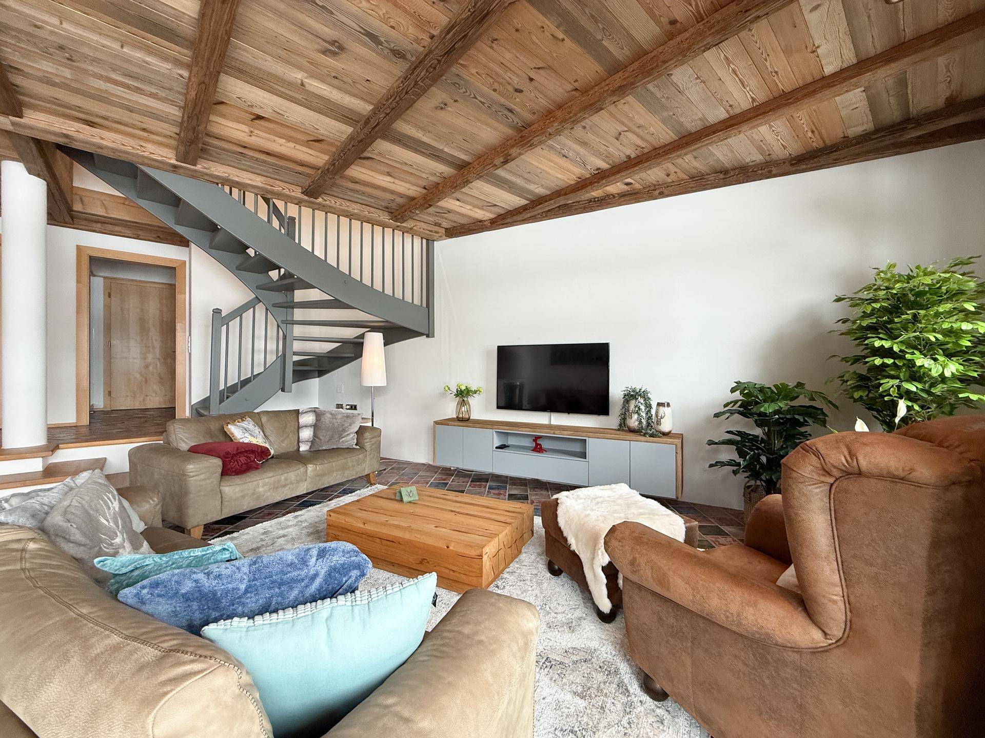 Gemütliches Wohnzimmer mit Holzbalkendecke, bequemen Sofas und einer modernen Wendeltreppe.