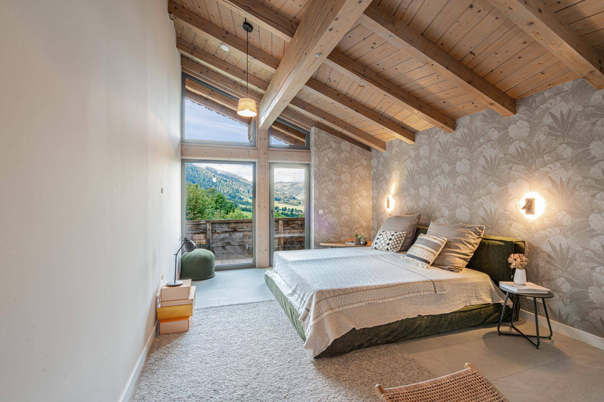 Gemütliches Schlafzimmer mit Holzbalkendecke, Tapete und großen Fenstern mit Bergblick.