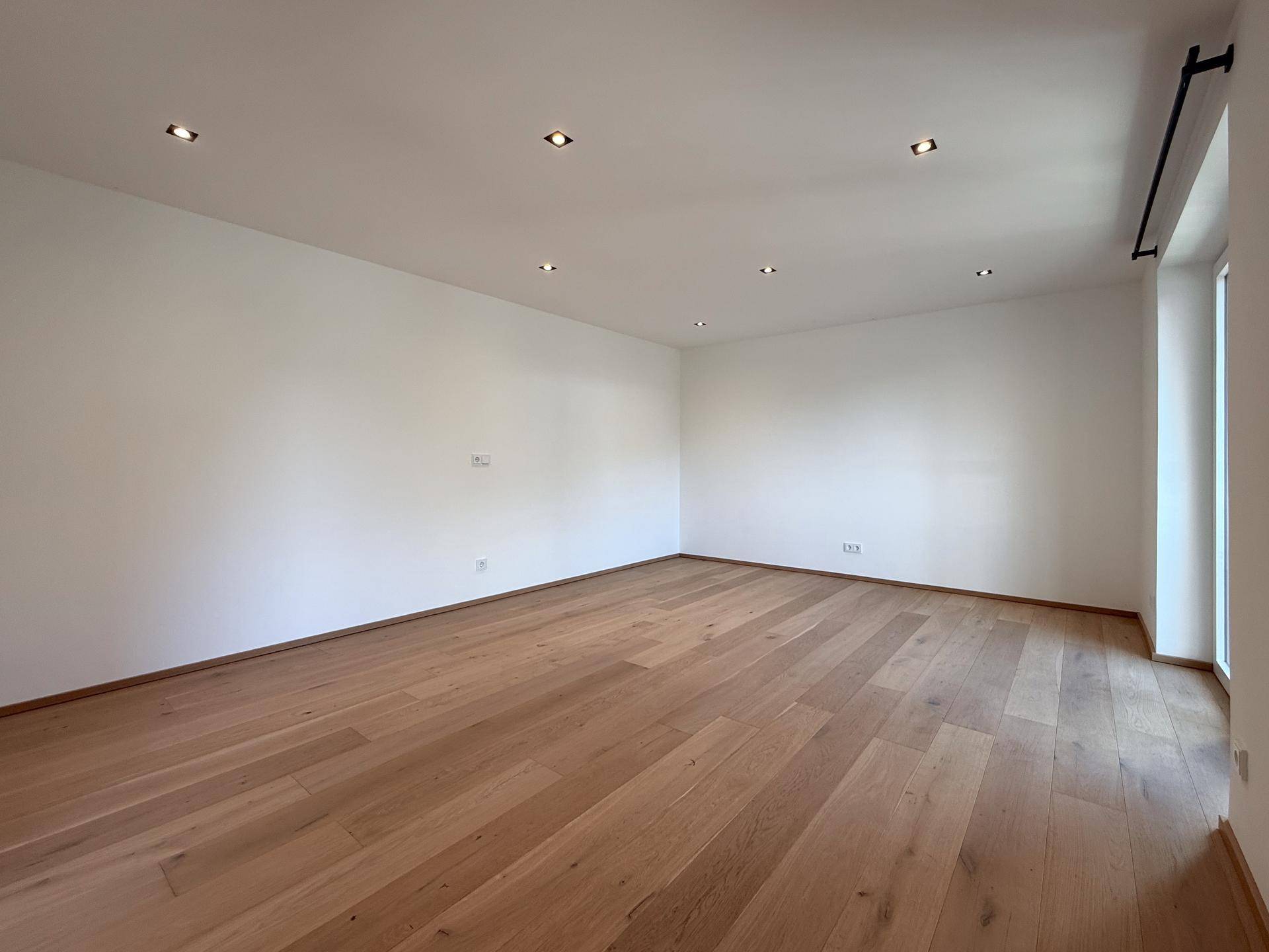 Geräumiger, leerer Raum mit Holzboden und Einbaustrahlern an der Decke.