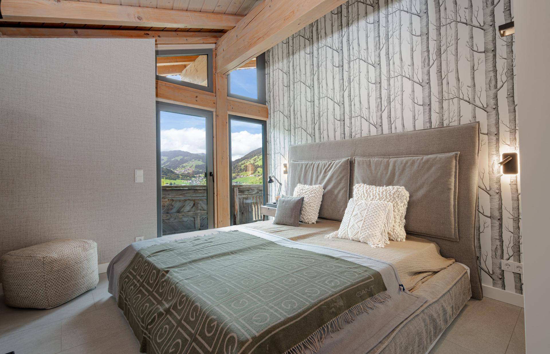 Helles Schlafzimmer mit Tapete im Birkenmuster, großem Bett und Zugang zum Balkon mit Bergblick.