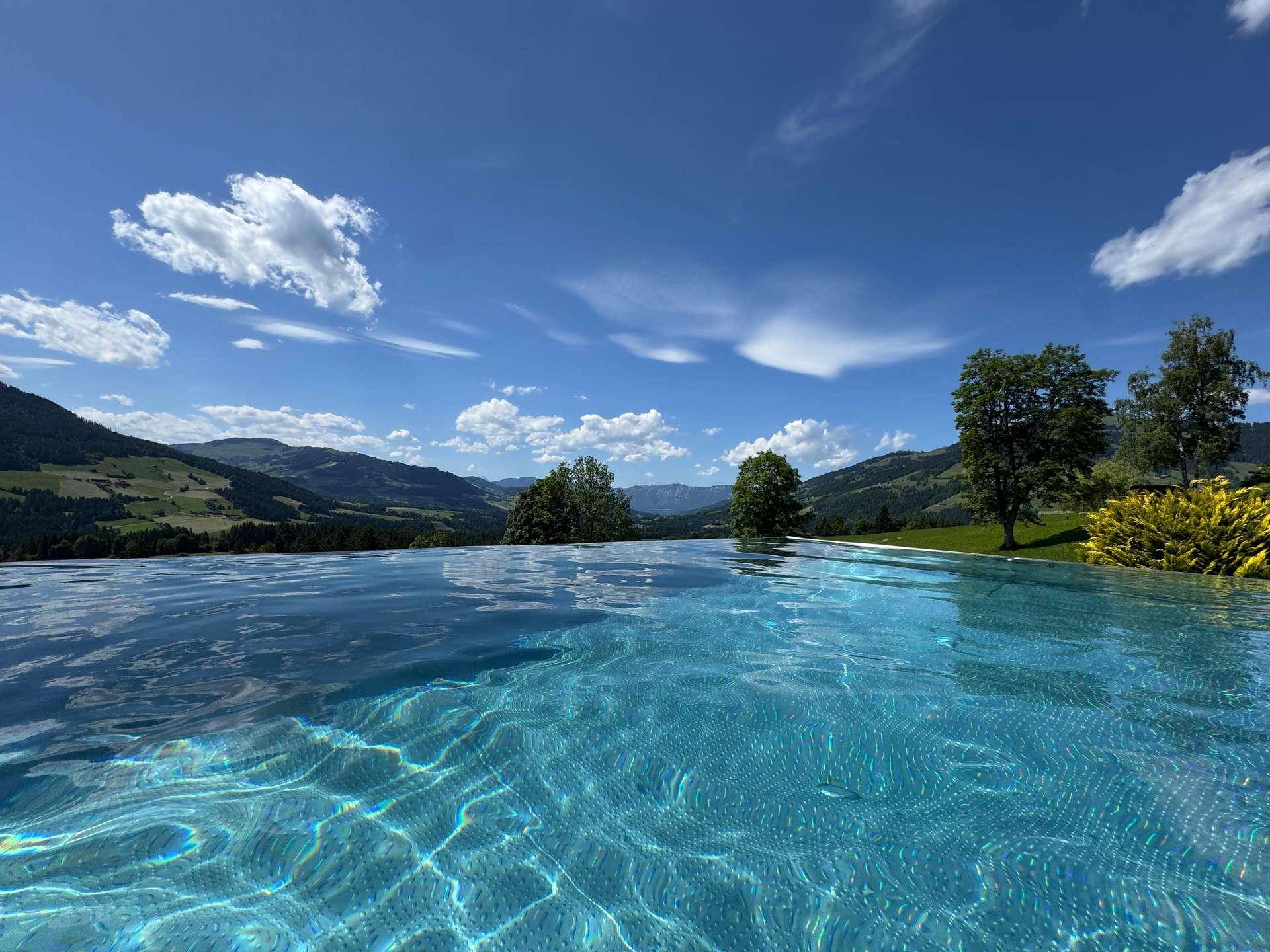 Weitläufiger Infinity-Pool mit spiegelnder Wasseroberfläche und beeindruckendem Blick auf die Alpen.