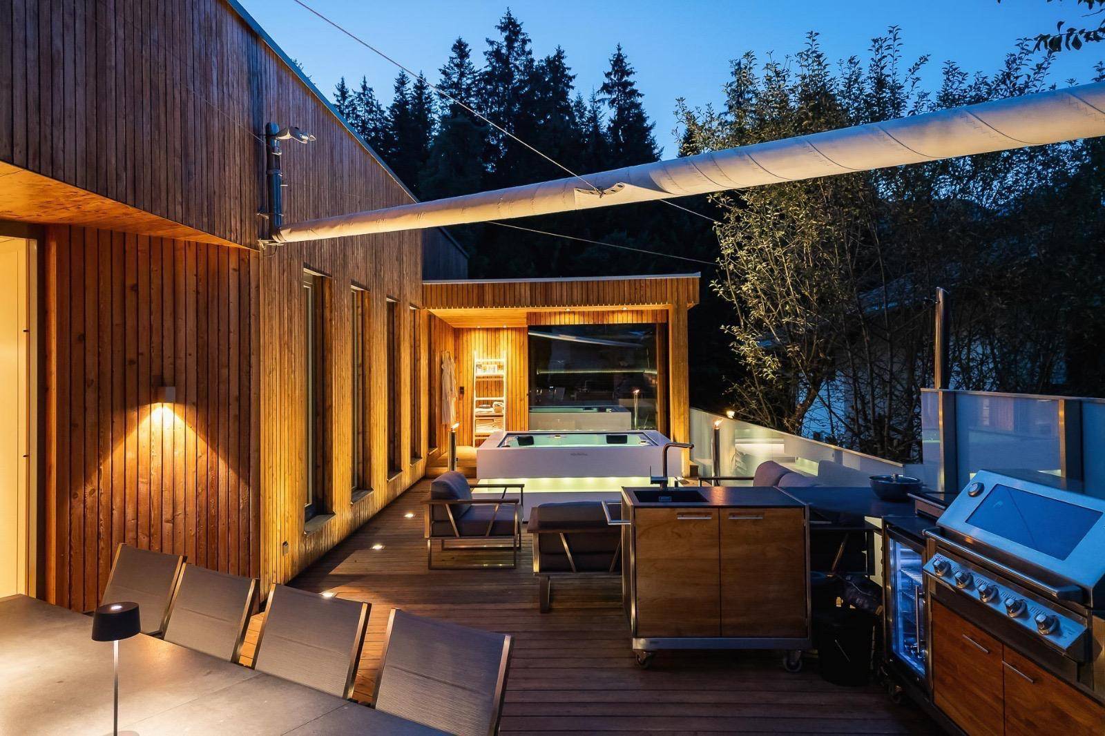 Weitläufige Holzterrasse mit Grillstation, Lounge-Möbeln und integriertem Whirlpool.