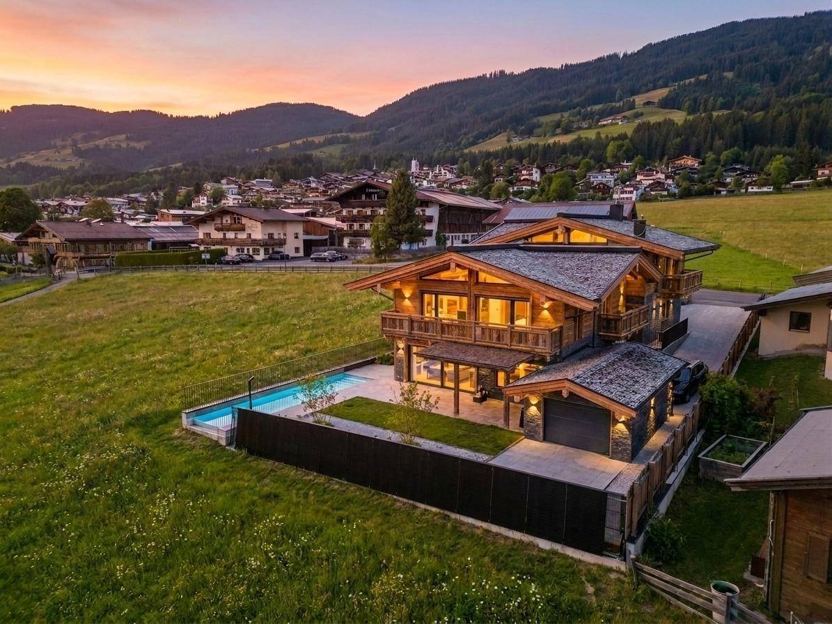 Luftaufnahme des luxuriösen Chalets mit Pool, umgeben von grünen Wiesen und einem Dorf.