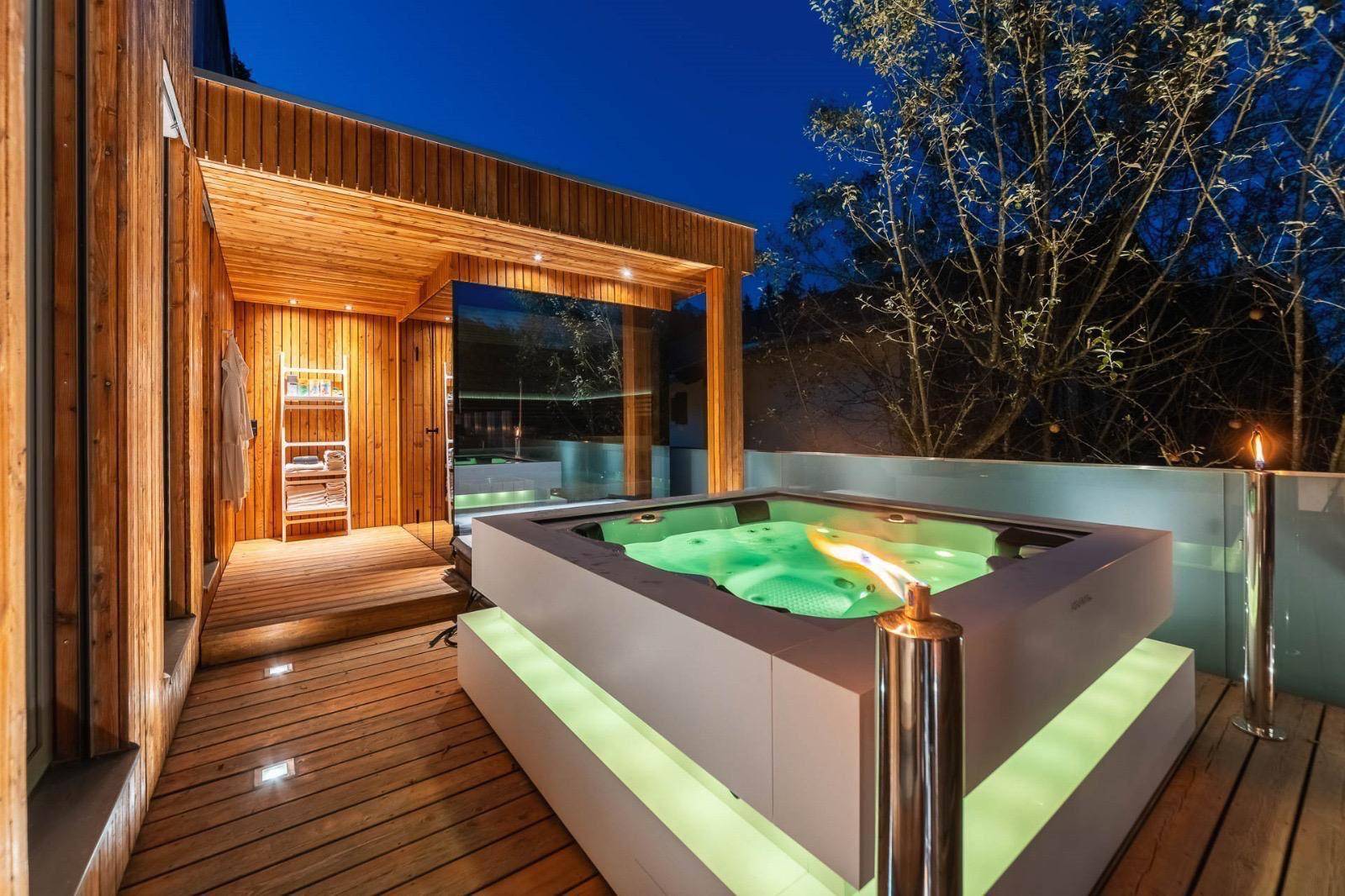 Luxuriöser Whirlpool auf der Holzterrasse mit stimmungsvoller Beleuchtung und Blick ins Grüne.