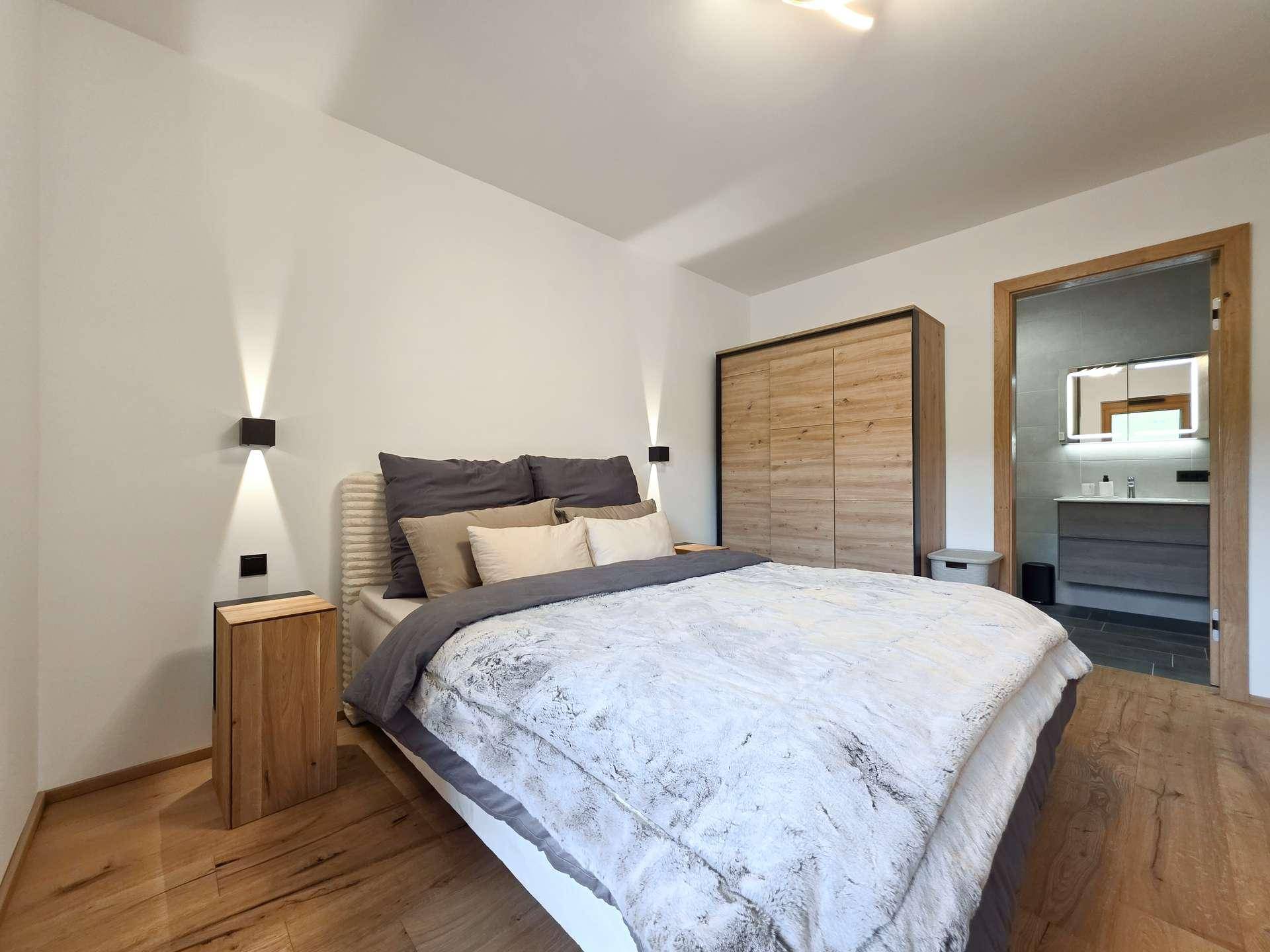 Gemütliches Schlafzimmer mit Holzboden und direktem Zugang zu einem modernen Badezimmer.