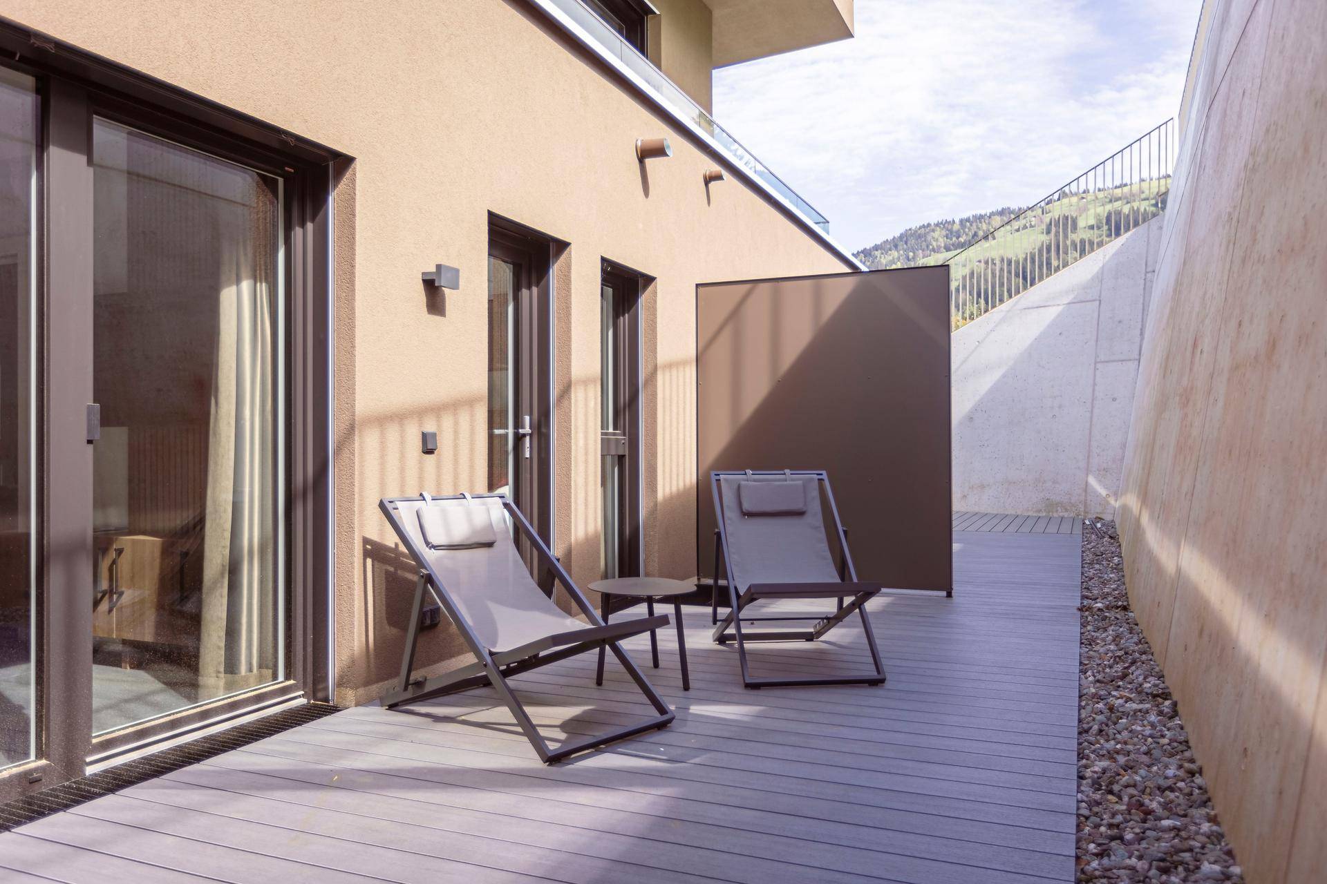 Ebenerdige Terrasse mit Holzdeck und bequemen Liegestühlen, umgeben von einer ruhigen Hanglandschaft.
