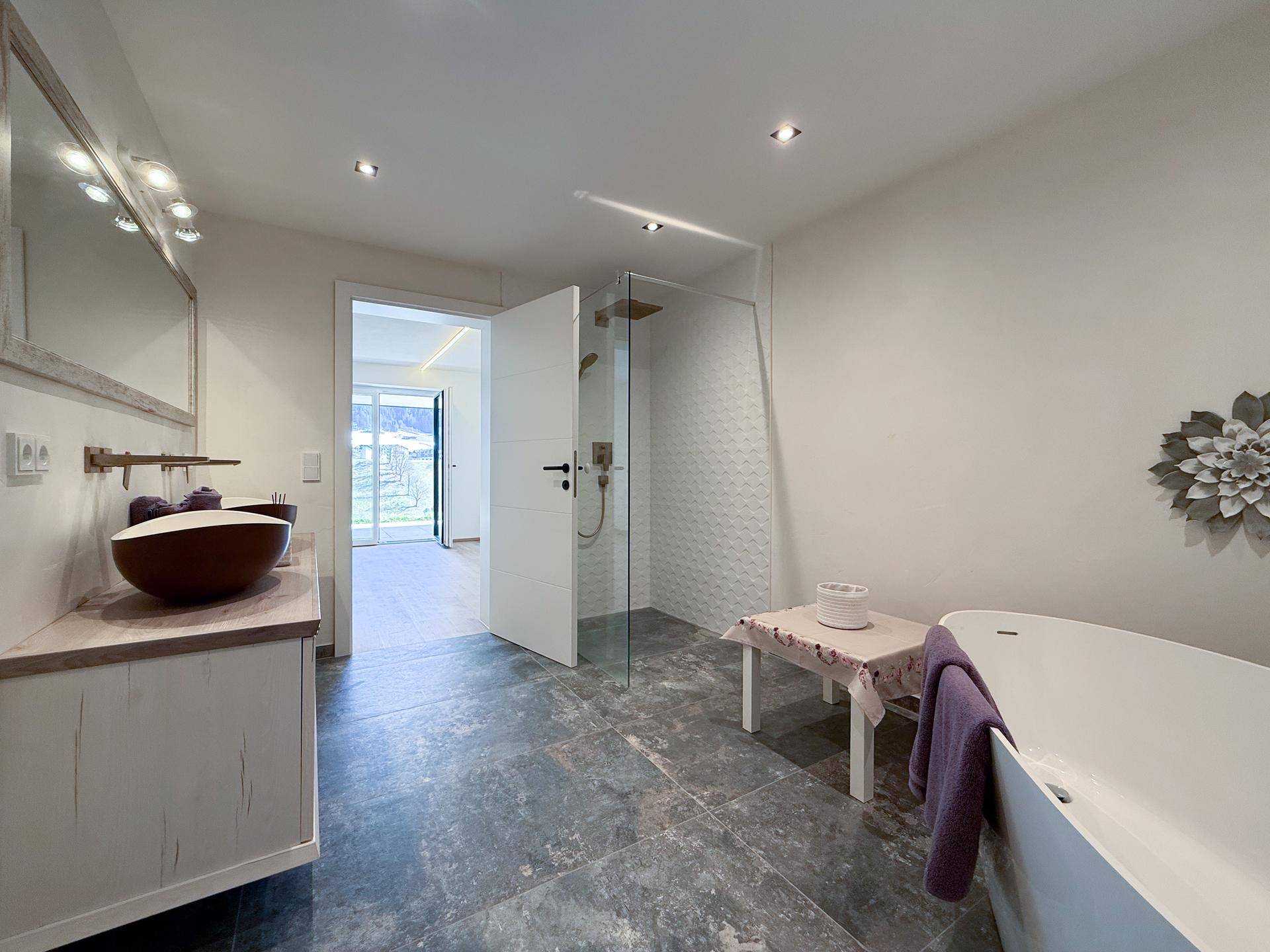 Modernes Badezimmer mit freistehender Badewanne, begehbarer Dusche und dunklen Fliesen.