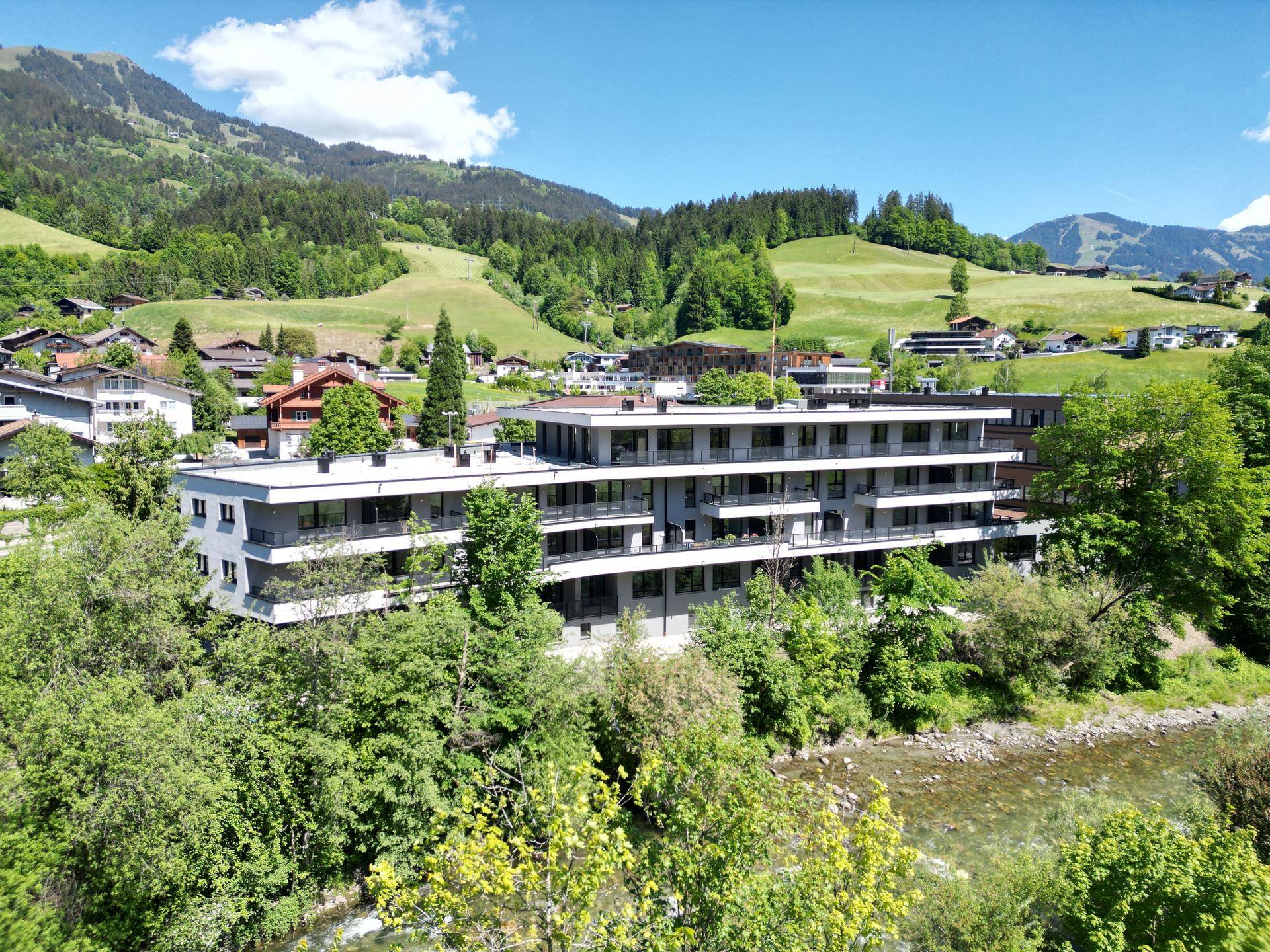 Luftaufnahme eines modernen Gebäudes am Flussufer mit Blick auf die umliegende Berglandschaft.