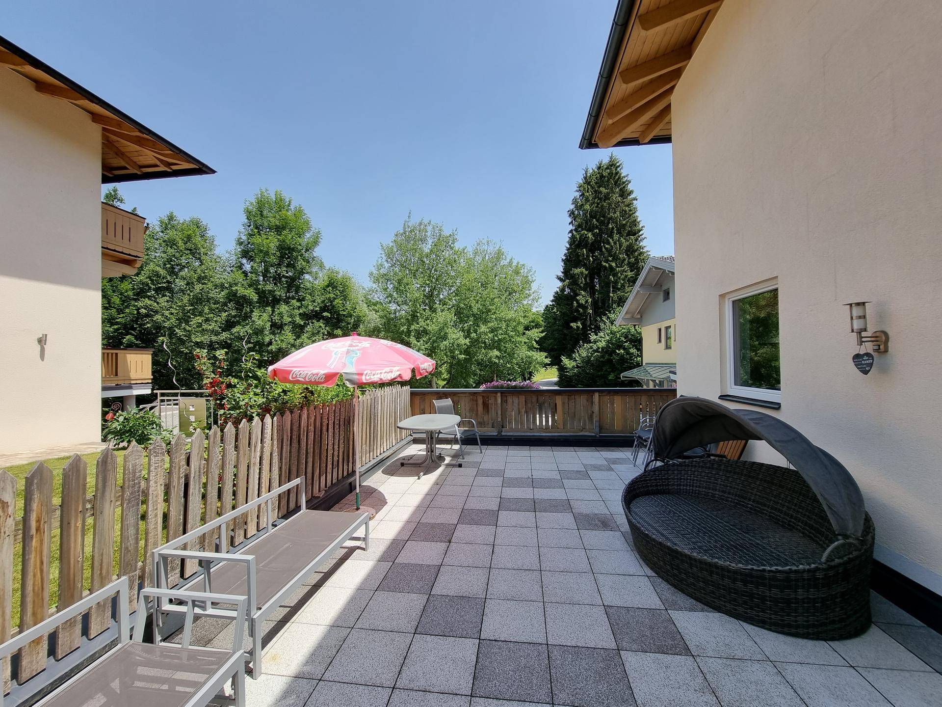 Geräumige Terrasse mit Fliesenboden, Sonnenliegen und einem schattenspendenden Sonnenschirm.