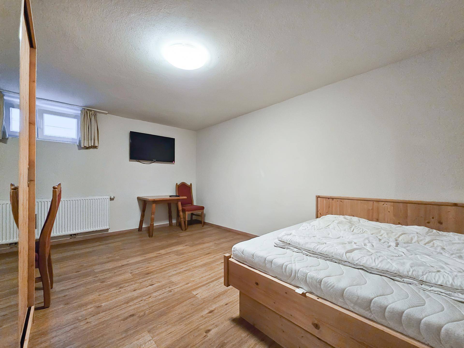 Gemütliches Schlafzimmer mit Holzbett, Parkettboden und kleinem Tisch mit Stühlen.