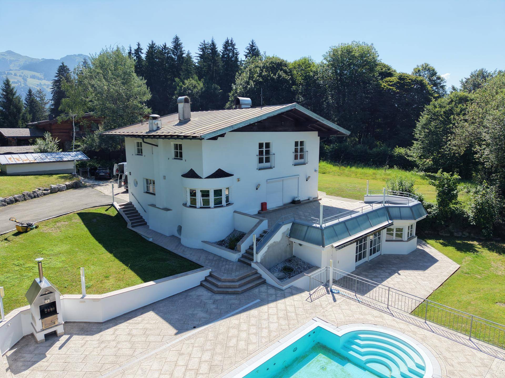 Frontansicht des Hauses mit großzügigem Poolbereich, Terrasse und Grillstelle im Freien.
