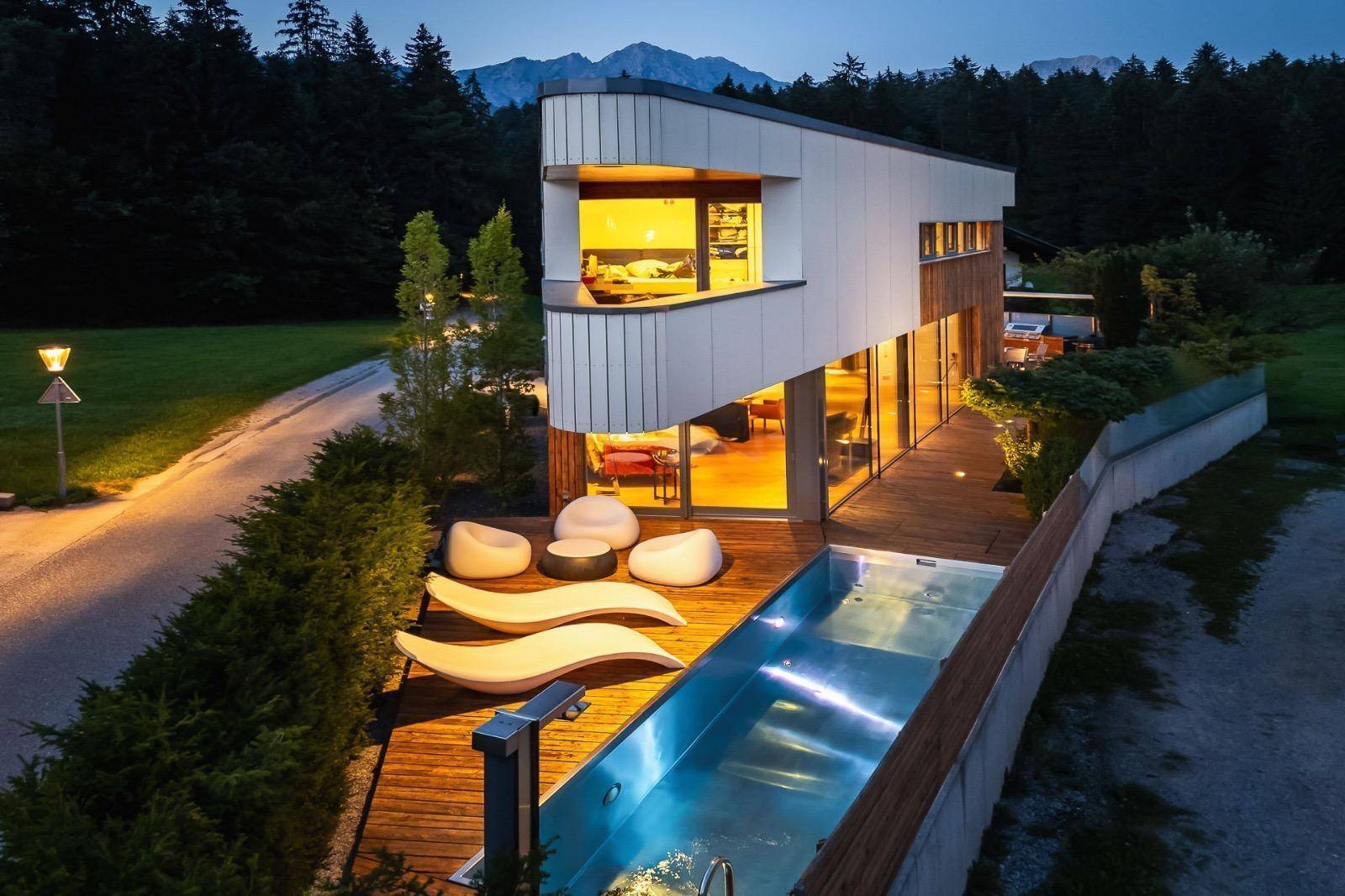 Außenansicht des modernen Hauses mit Pool, Holzdeck und Liegen, umgeben von Wald und Natur.