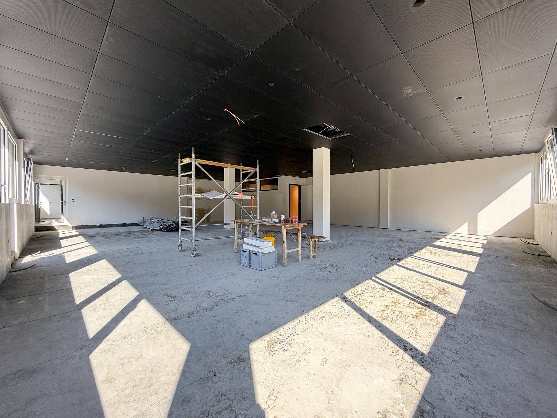 Großer, heller Gewerberaum mit Betonboden, dunkler Decke und viel Tageslicht, noch im Bau.