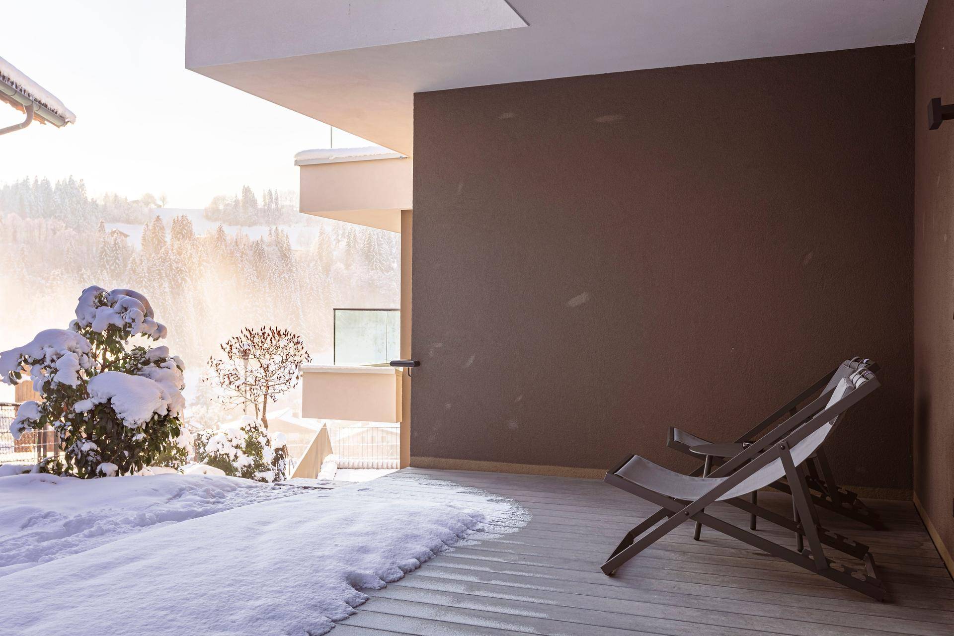 Winterliche Terrasse mit Schnee und Liegestühlen, bietet einen ruhigen Blick auf die verschneite Landschaft.