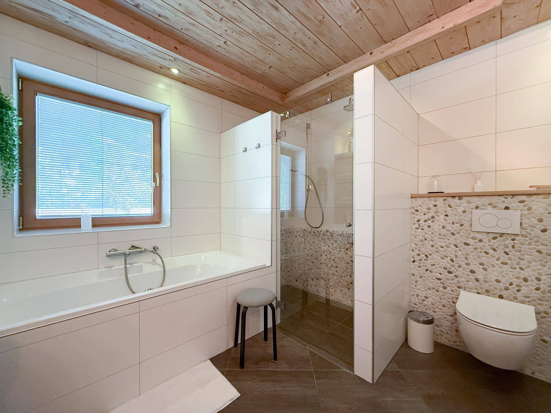 Helles Badezimmer mit Badewanne, begehbarer Dusche und Wand-WC.