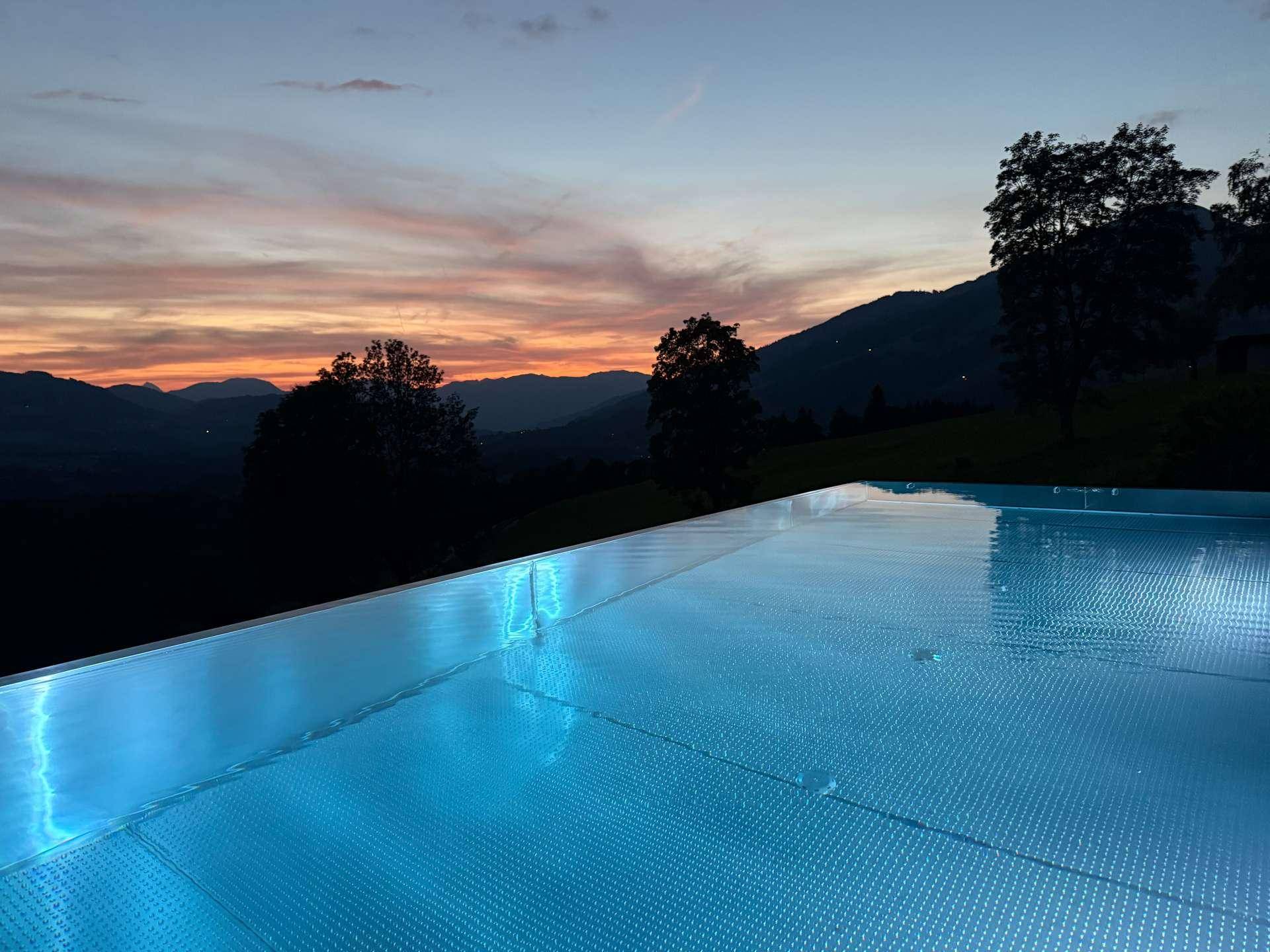 Infinity-Pool bei Sonnenuntergang mit leuchtendem Wasser und malerischem Bergblick.