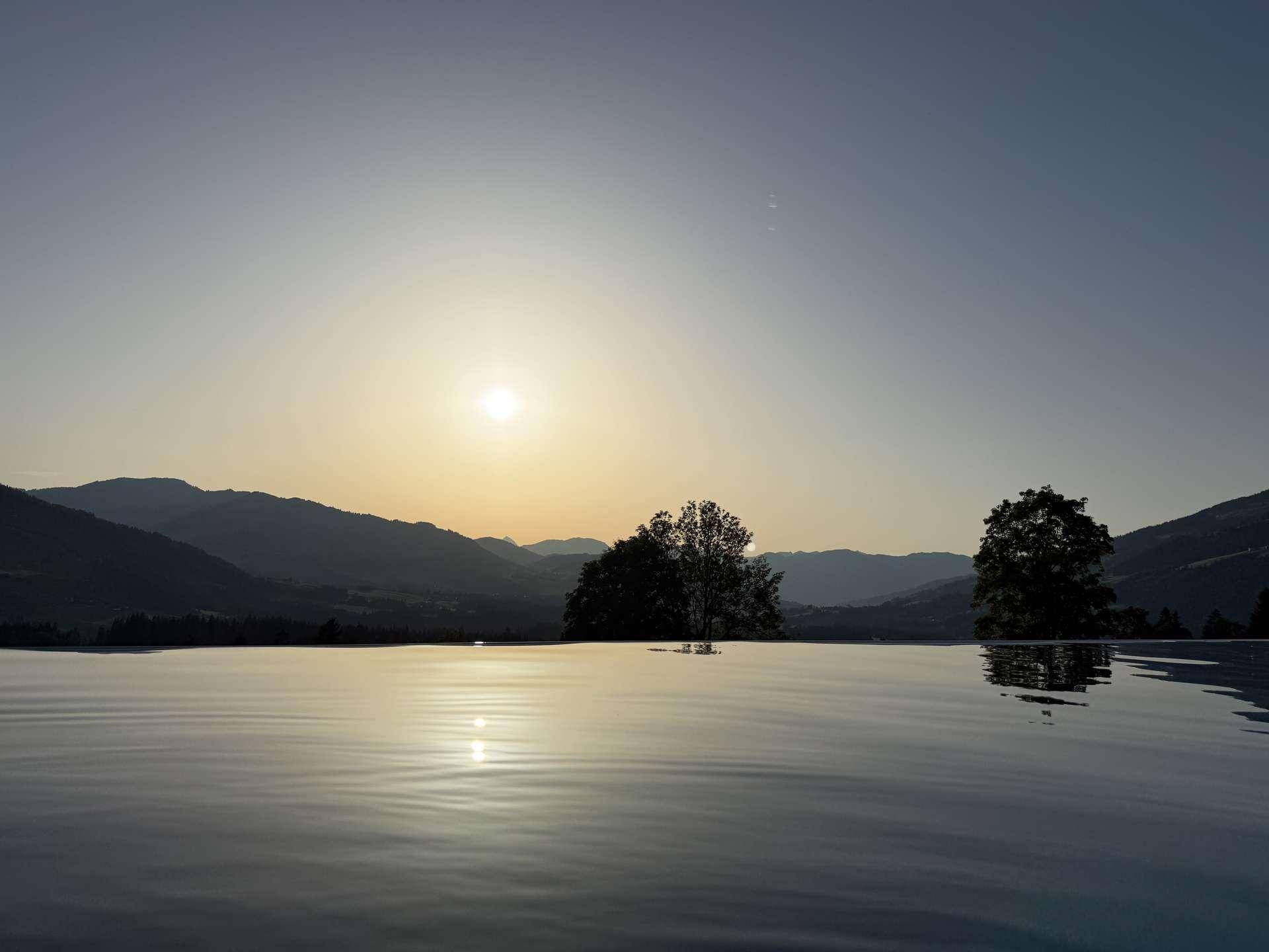 Ruhiger Infinity-Pool bei Sonnenuntergang mit spiegelnder Wasseroberfläche und Bergblick.