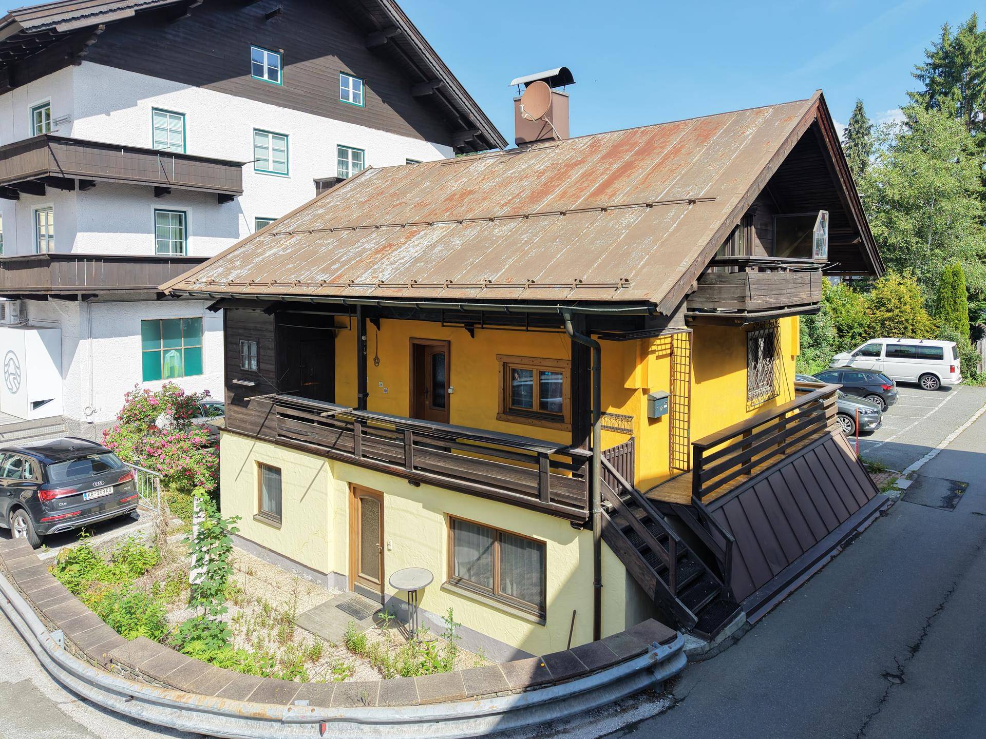 Traditionelles Haus mit gelber Fassade, Holzbalkonen und Außentreppe in alpiner Umgebung.