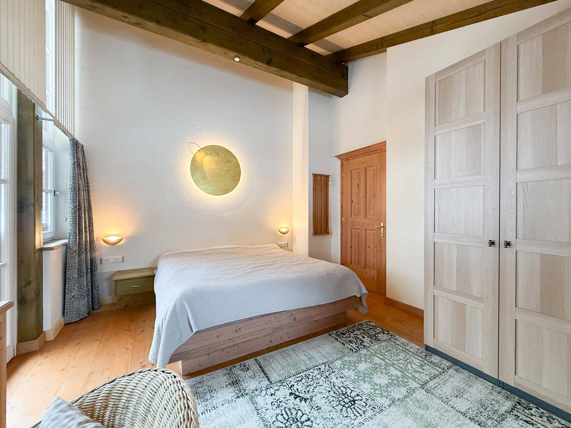 Schlafzimmer mit Holzbalkendecke, Doppelbett und großem Kleiderschrank aus hellem Holz.