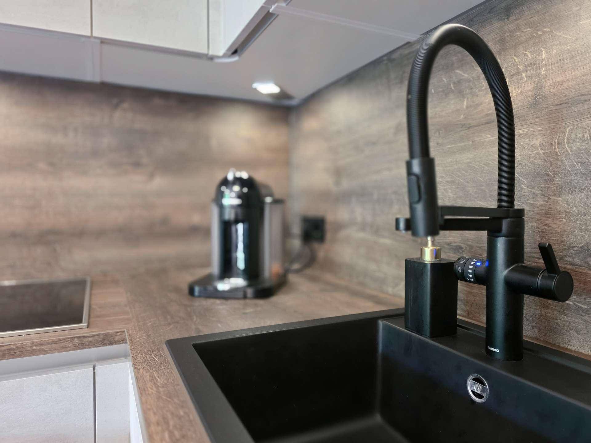 Detailansicht der modernen Küchenspüle mit schwarzem Wasserhahn und Kaffeemaschine.