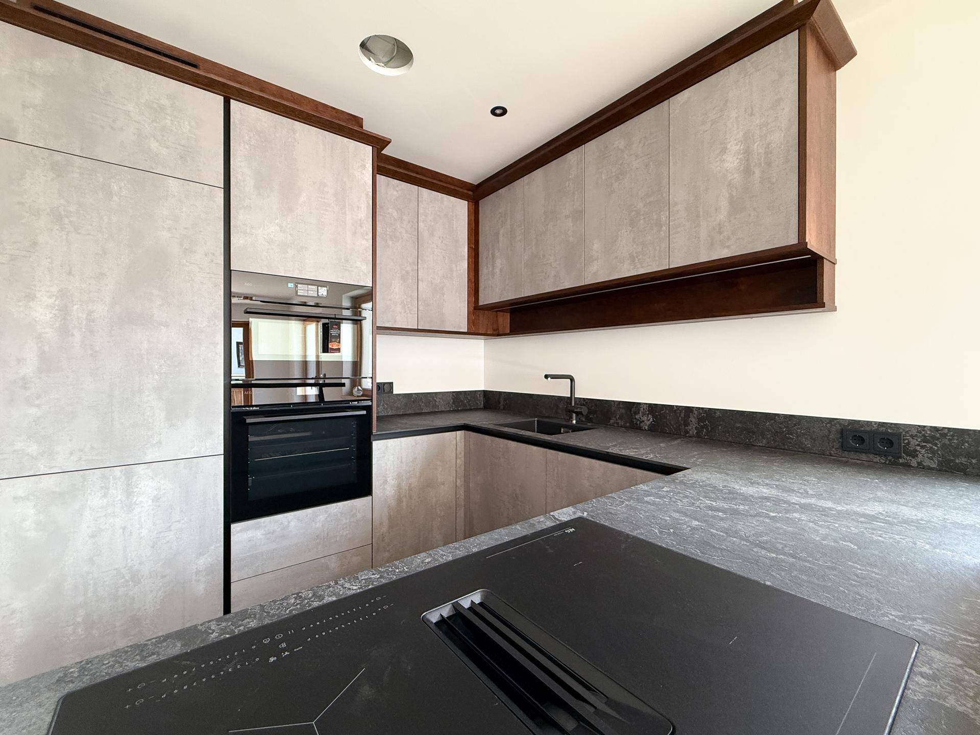 Moderne Küche mit dunklen Arbeitsplatten, integriertem Kochfeld und Backofen in zeitgemäßem Design.