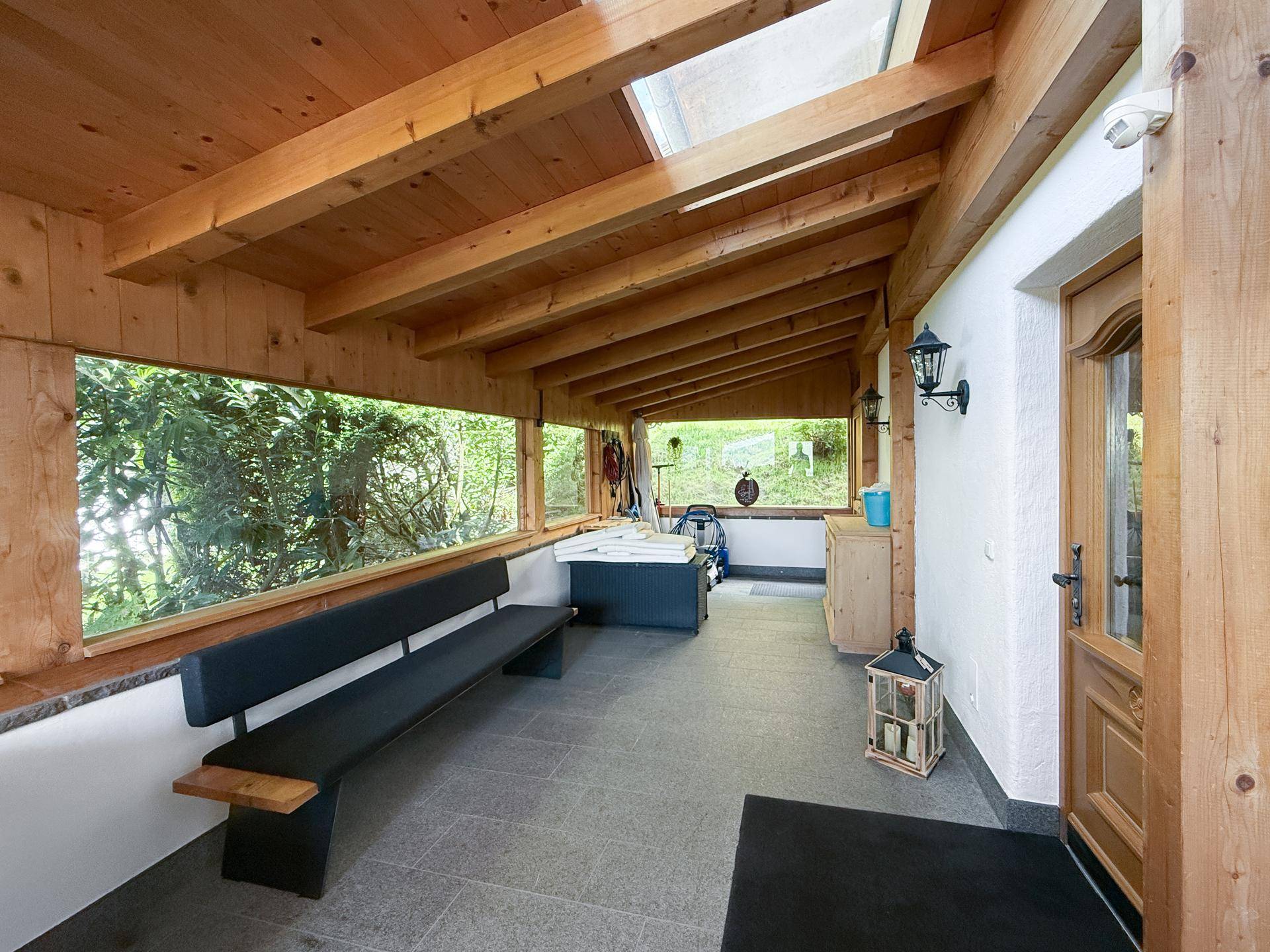 Überdachte Loggia mit Sitzbank, Holzbalken und Blick ins Grüne.