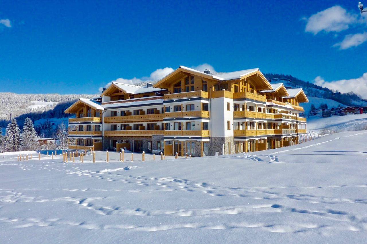 Attraktives Mehrfamilienhaus in alpiner Architektur, umgeben von verschneiter Winterlandschaft.
