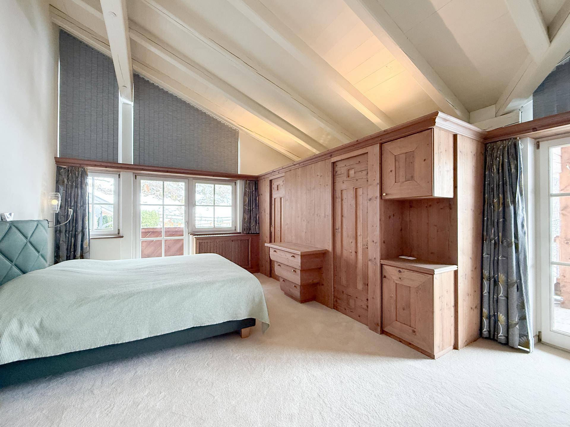 Schlafzimmer mit Dachschräge, Einbauschränken aus Holz und Zugang zum Balkon.