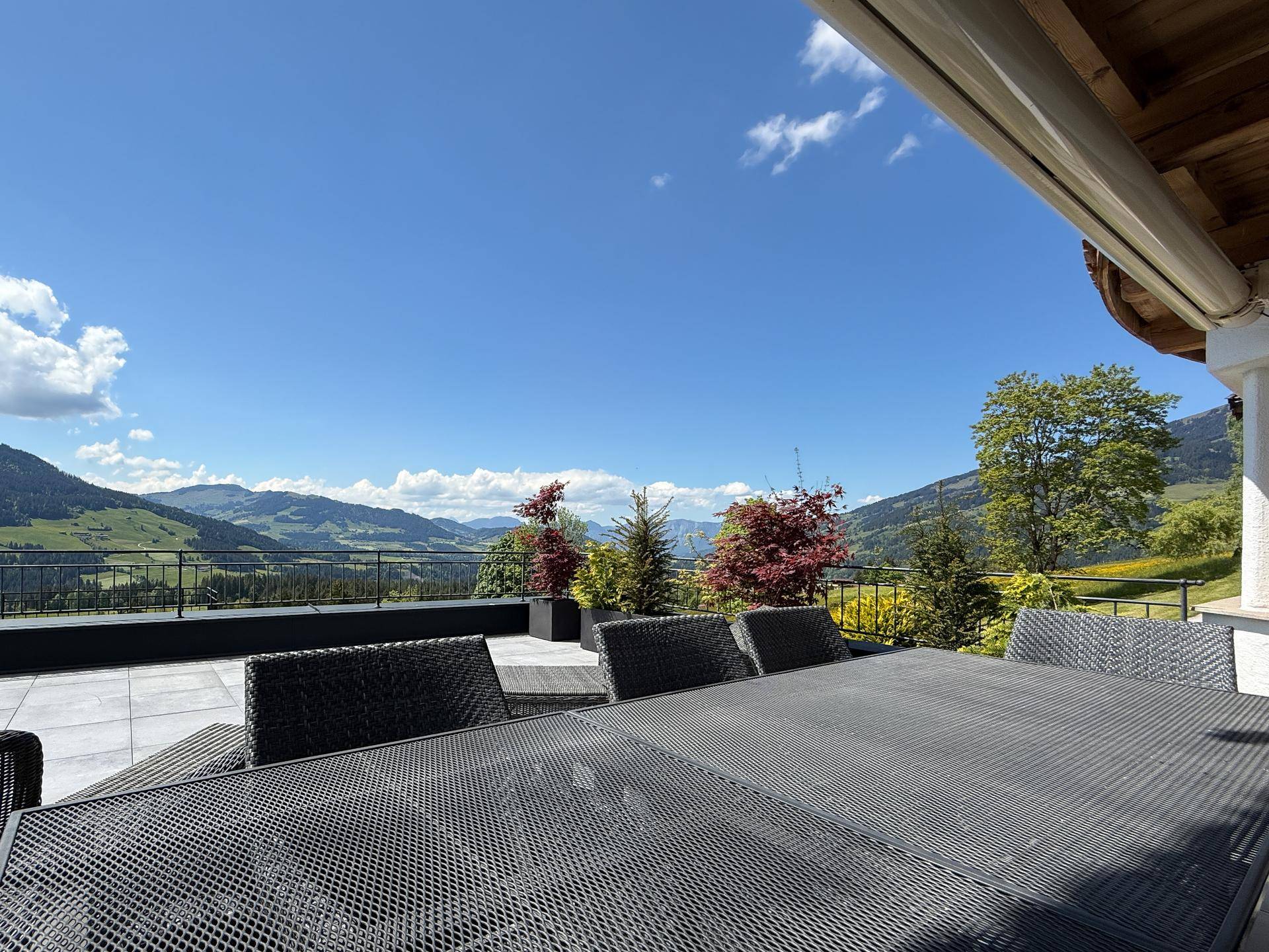 Große Sonnenterrasse mit Esstisch und Stühlen, umgeben von einer malerischen Berglandschaft.