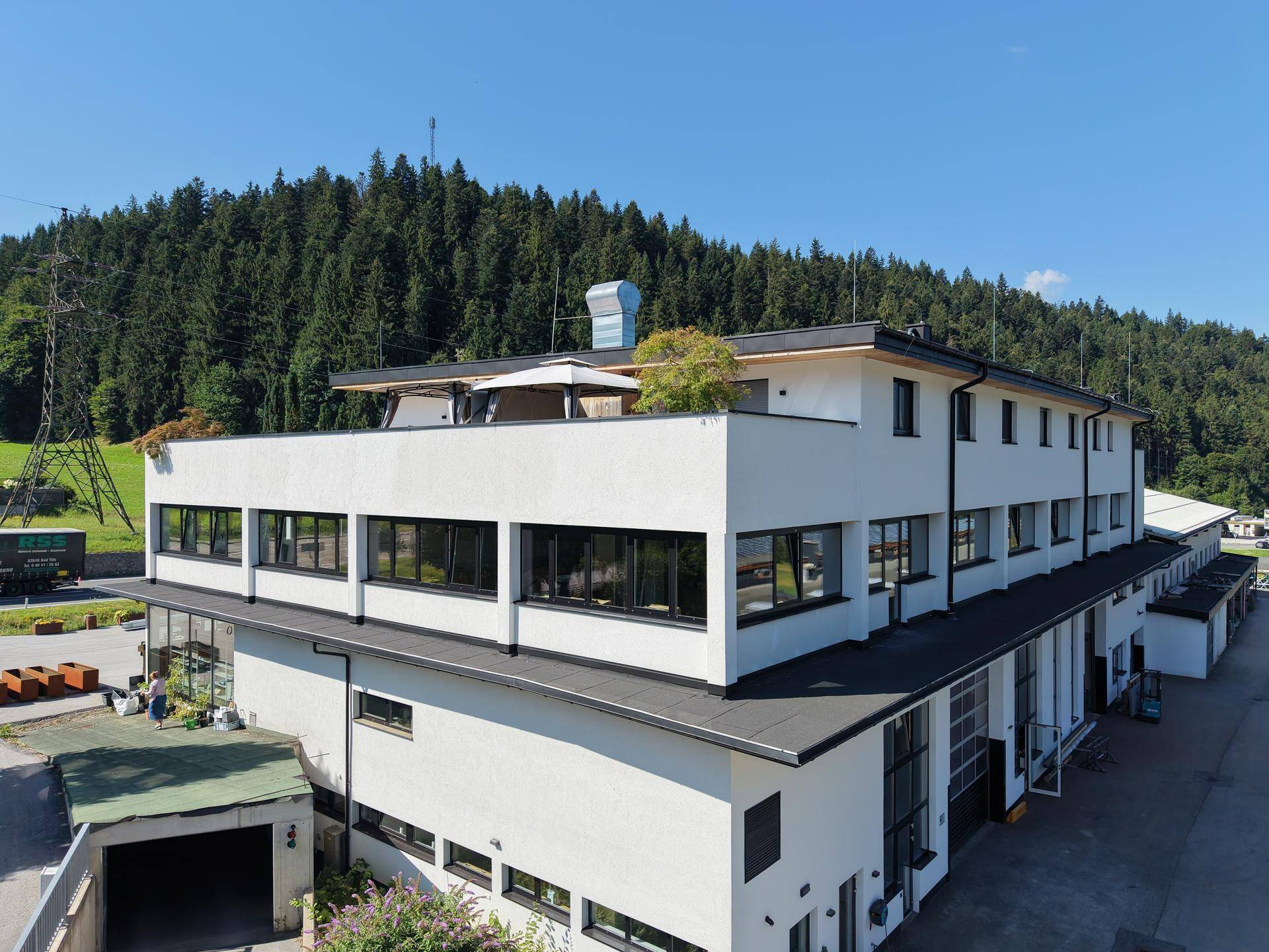 Luftaufnahme des modernen Geschäftsgebäudes mit weißer Fassade und Flachdach, eingebettet in grüne Hügel.