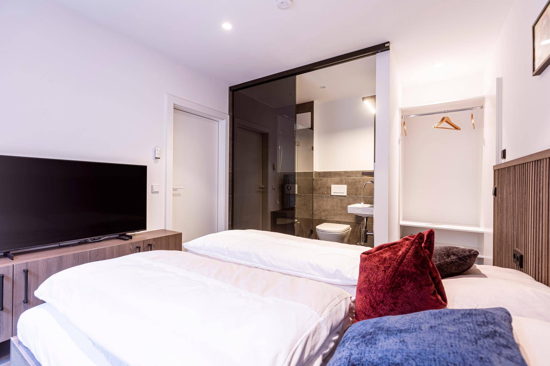 Schlafzimmer mit Doppelbett und integriertem Badezimmer, abgetrennt durch eine Glaswand.
