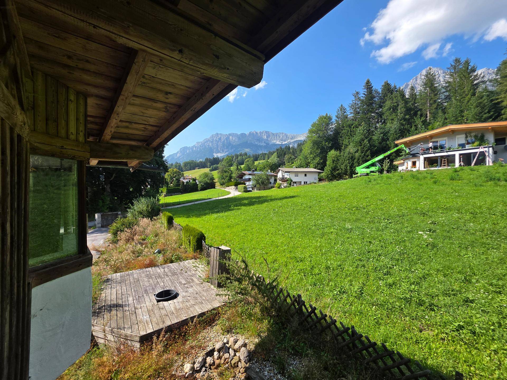 Panoramablick von einem Balkon über grüne Hügel, andere Häuser und die umliegenden Berge.