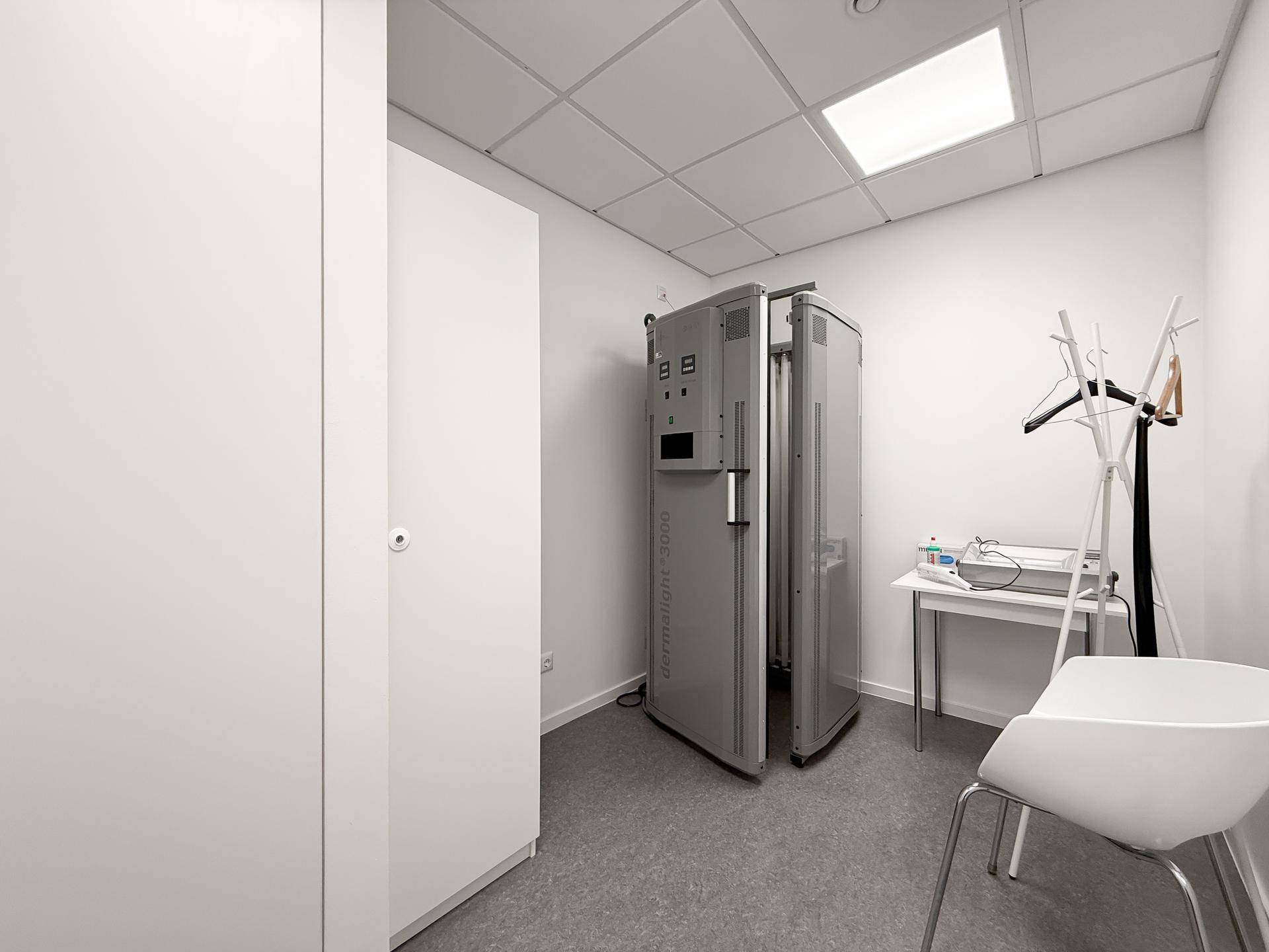 Kleiner Behandlungsraum mit vertikalem Therapiegerät, integriertem Schrank und Garderobe.