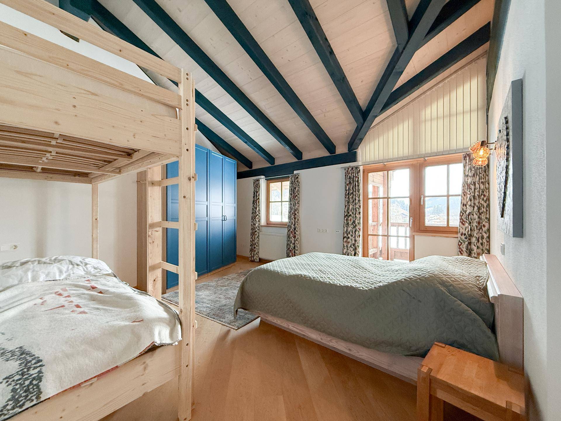 Geräumiges Schlafzimmer mit Holzbalkendecke, Etagenbett und großen Fenstern mit Bergblick.